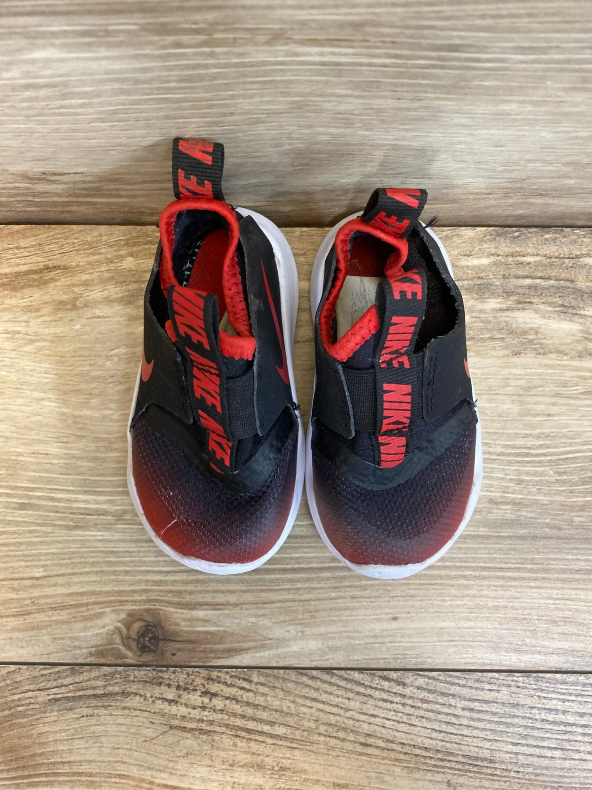 Top view of Flex Runner TD toddler sneakers in University Red Black, showcasing slip-on design on a wood floor