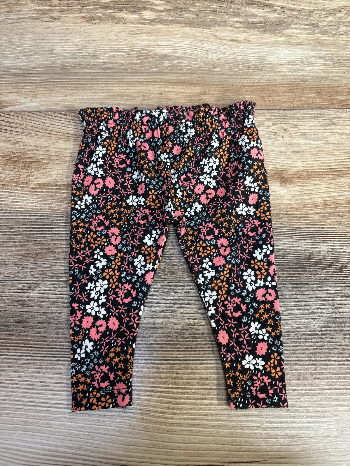 Girls' floral print leggings with pink, white, and orange flowers on black, displayed on wooden floor
