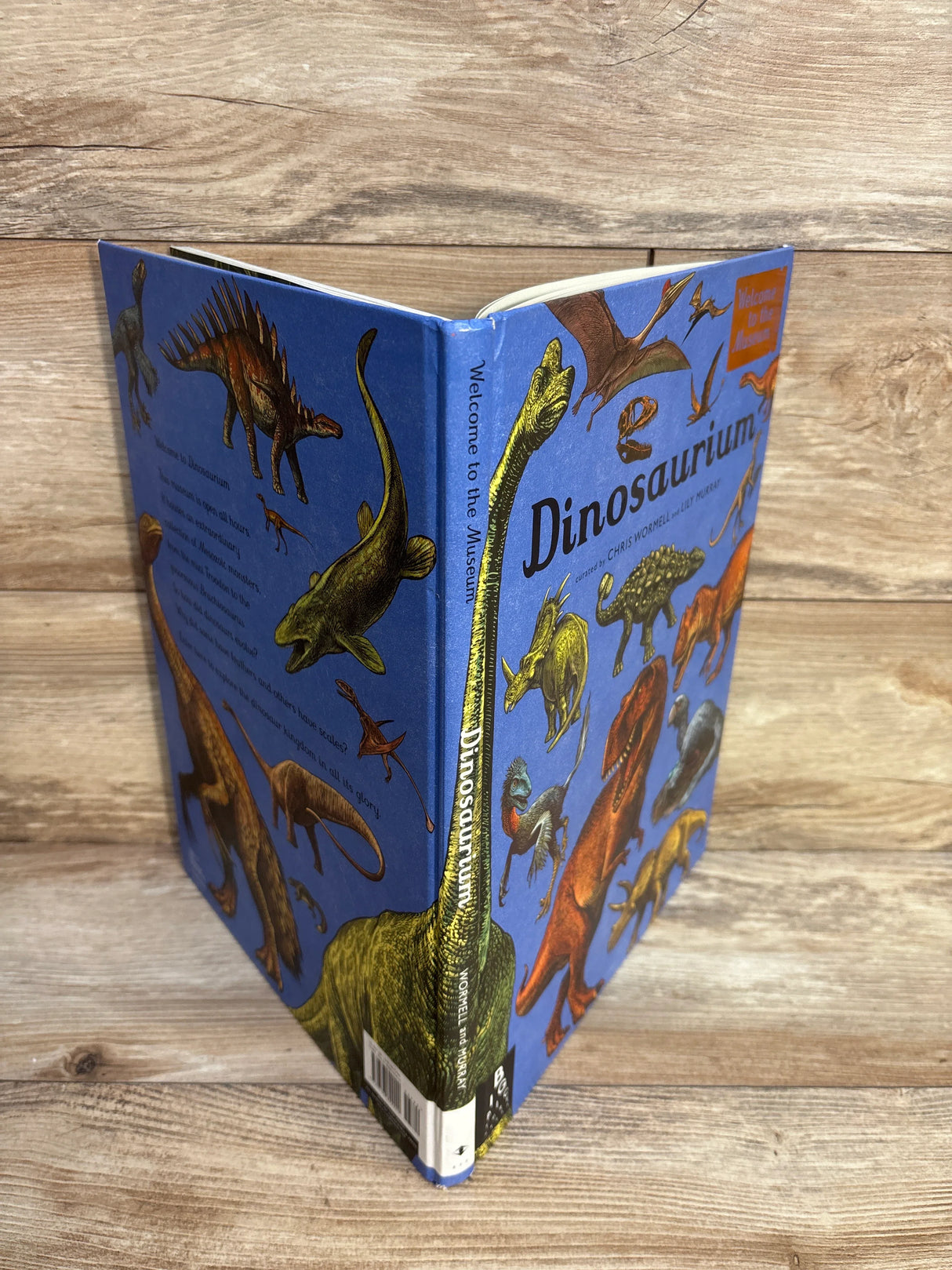 Dinosaurium hardcover book with illustrated dinosaurs on blue cover, standing on wood surface
