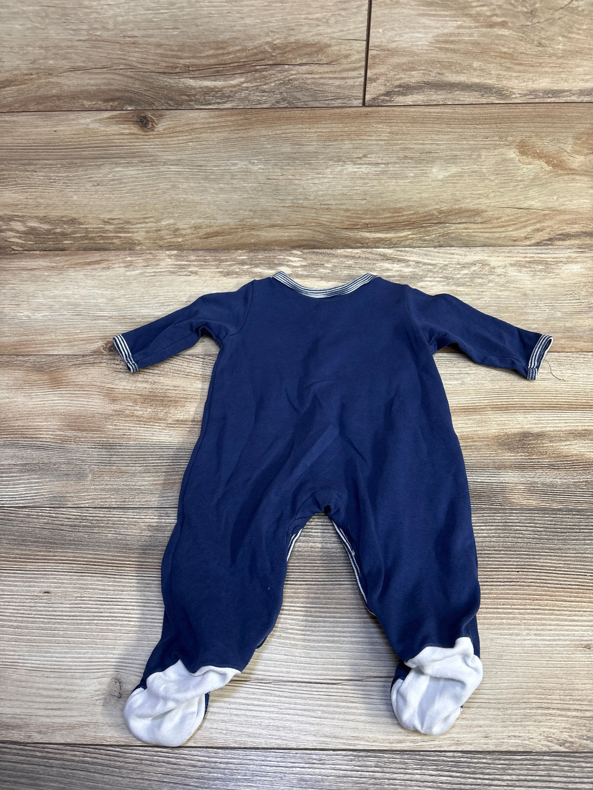 Back view of Little Me navy footed sleeper showing striped collar and cuffs on wood background