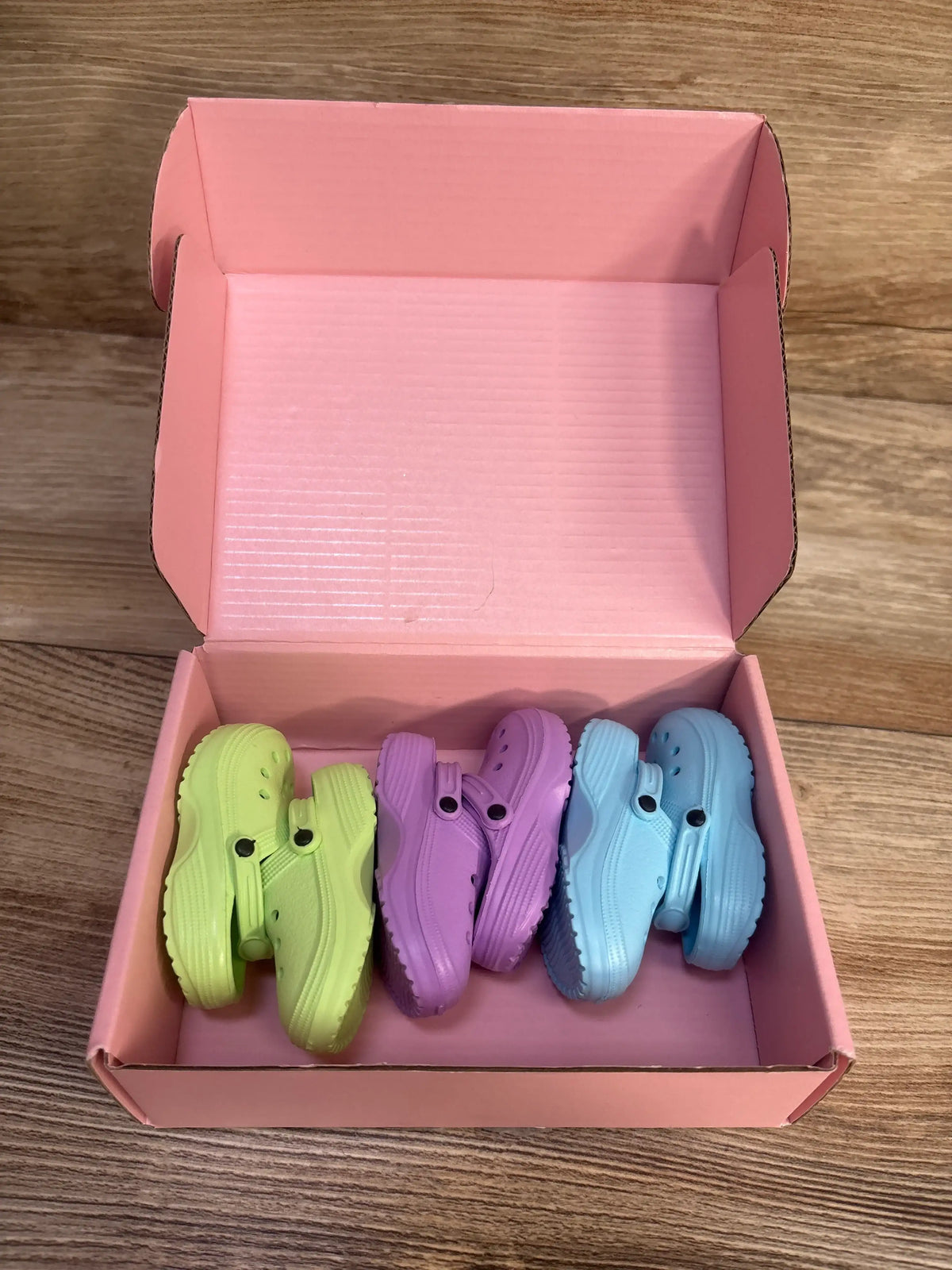 Top view of HXIELEC 3pk clog shoes for dolls in lime green, purple, and blue inside an open pink box