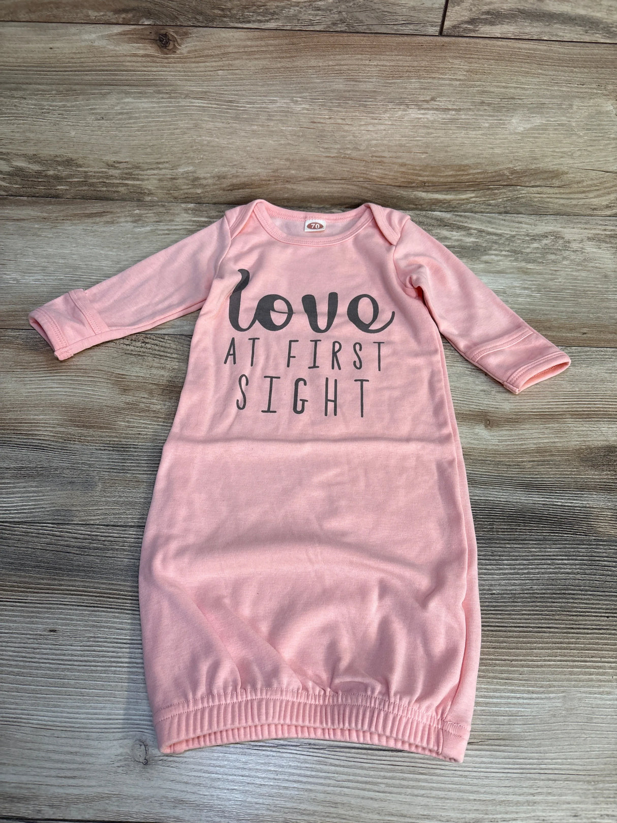 Pink baby gown with 'love at first sight' text, long sleeves, laid flat on wood floor