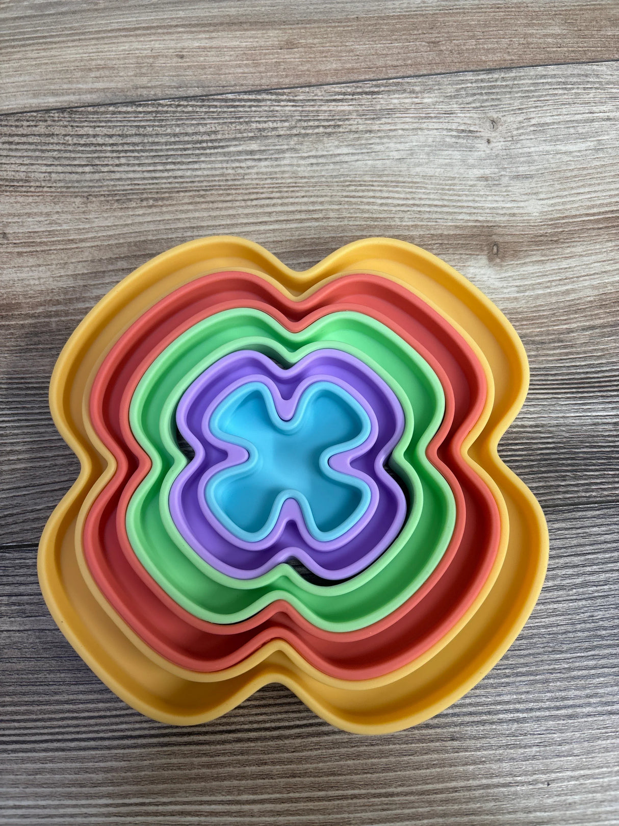 Set of colorful flower-shaped nesting silicone bowls in blue, purple, green, red, and yellow on wooden background