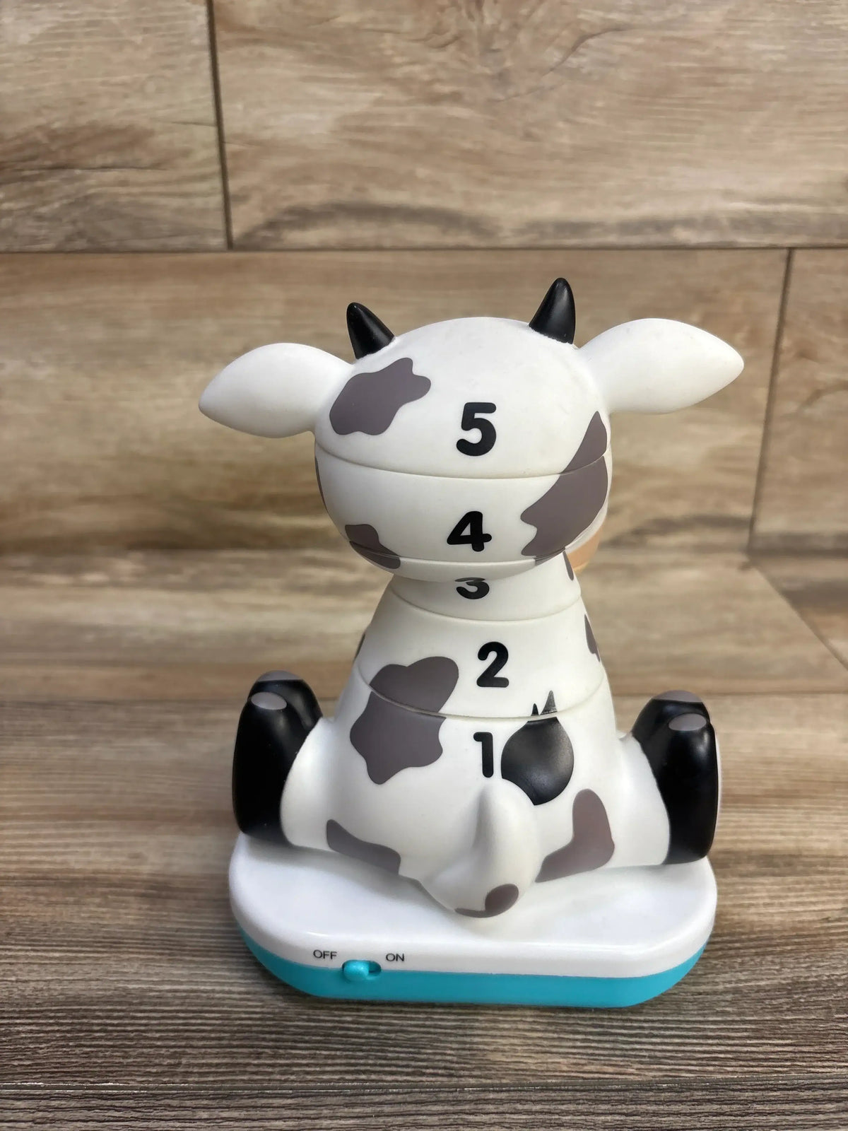Back view of Stack-a-Roos Baby Cow showcasing numbered 1-5 stackable sections, gray spots and teal base on wood tabletop