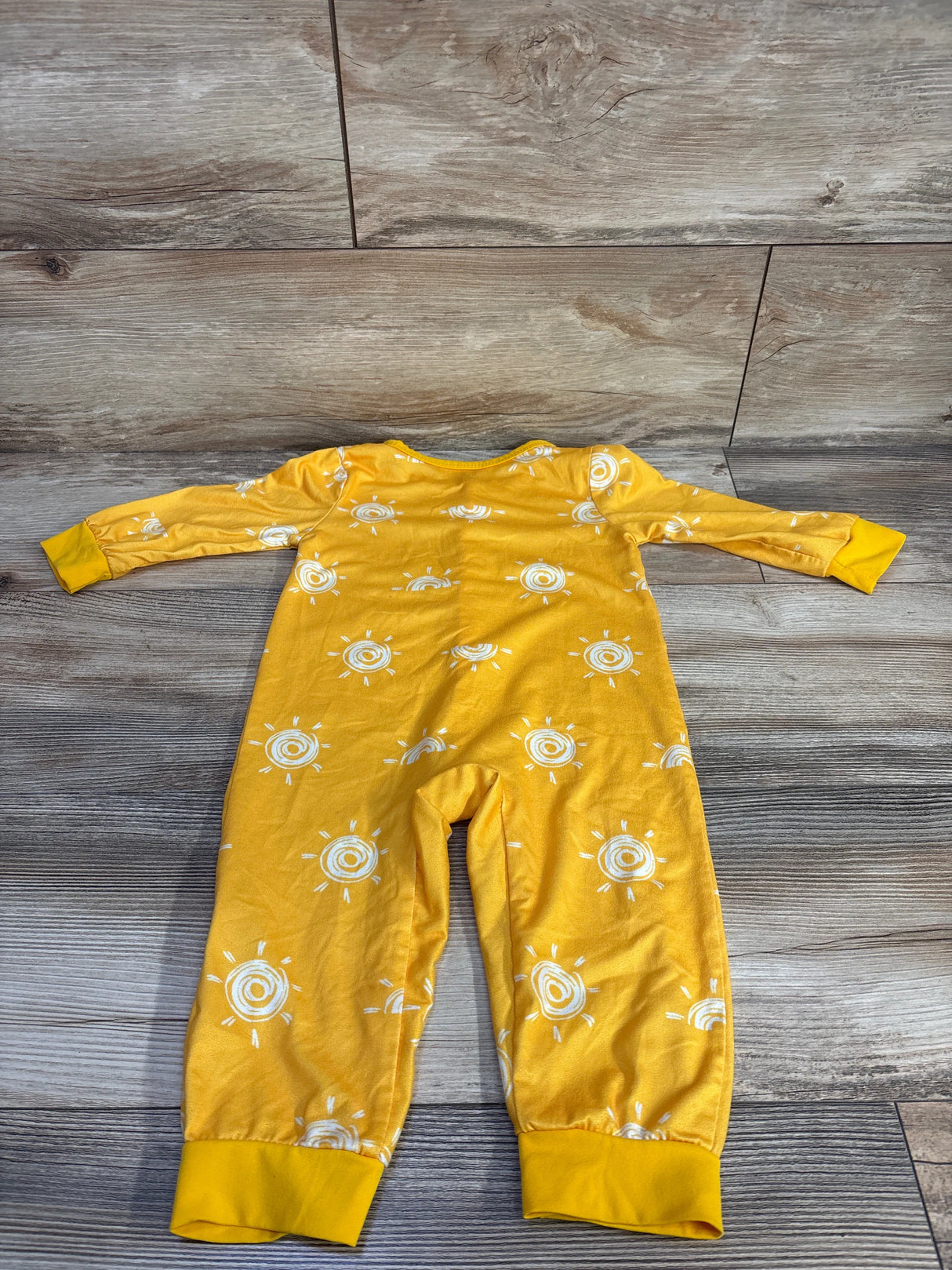 Flat-lay back view of yellow snap jumpsuit size 9-12 months showing white sun print and ribbed cuffs on wood background