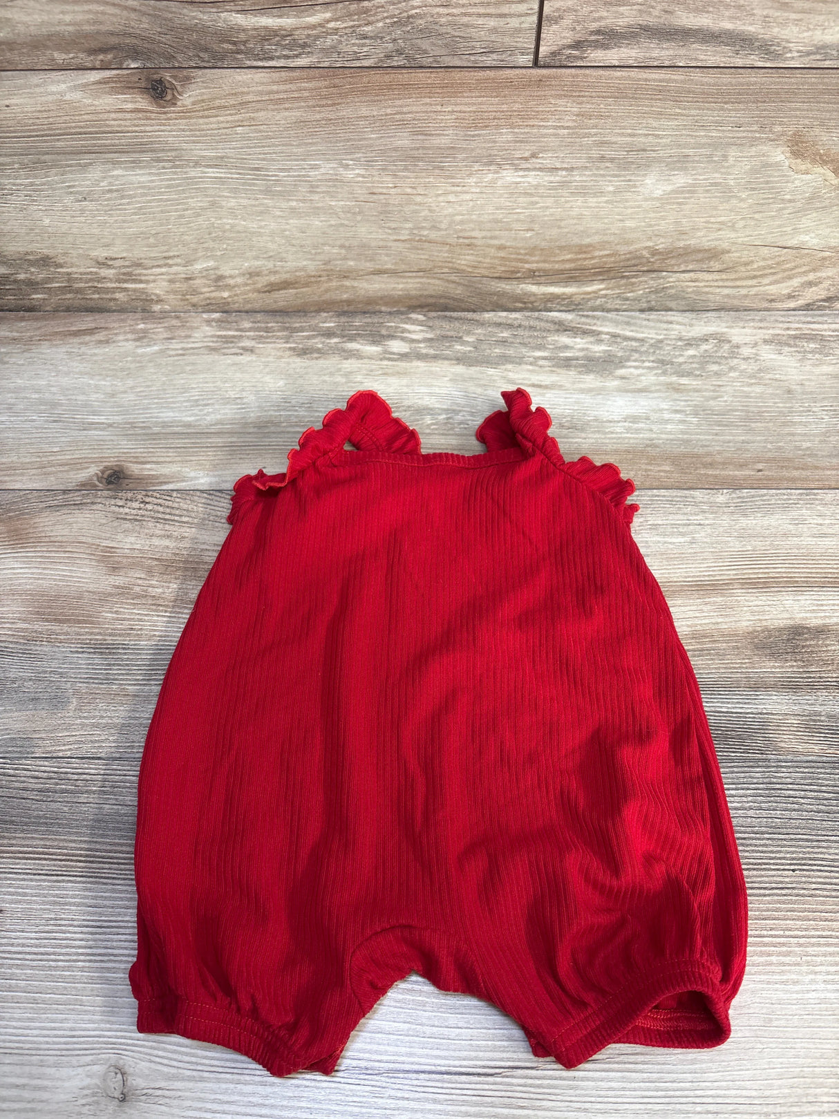 Flat lay of red Disney Baby Minnie Mouse shortie romper (6-9m) showing ruffled shoulder straps and gathered elastic leg openings on light wood background