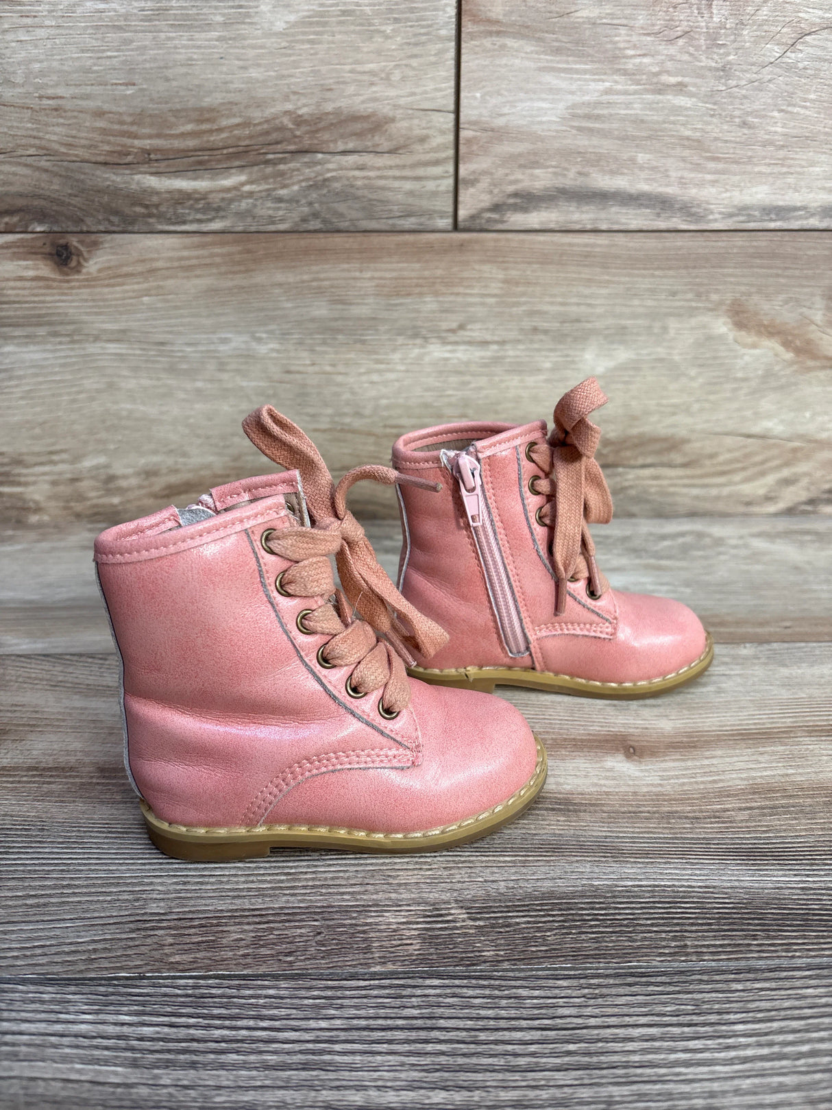 Pair of pink toddler leather lace-up boots with side zipper on wooden floor