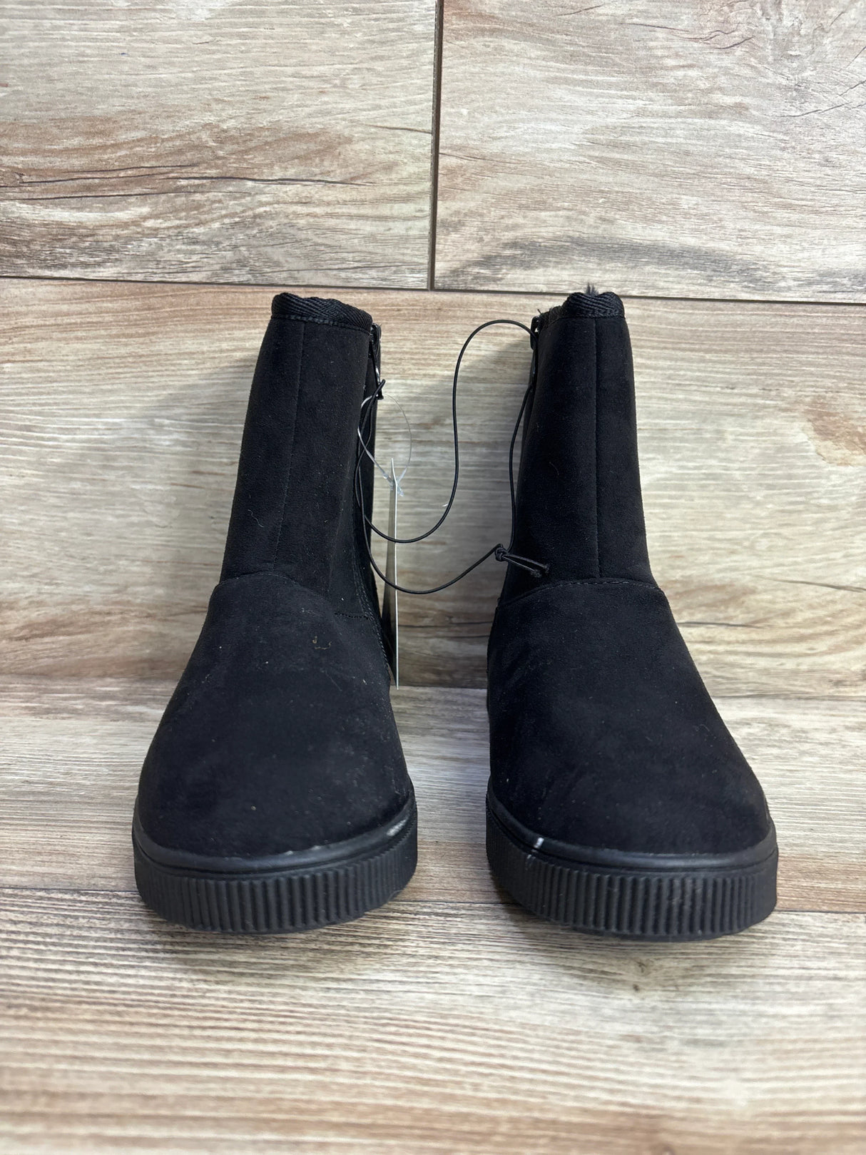 Pair of black suede kids ankle boots with side zippers on wood floor