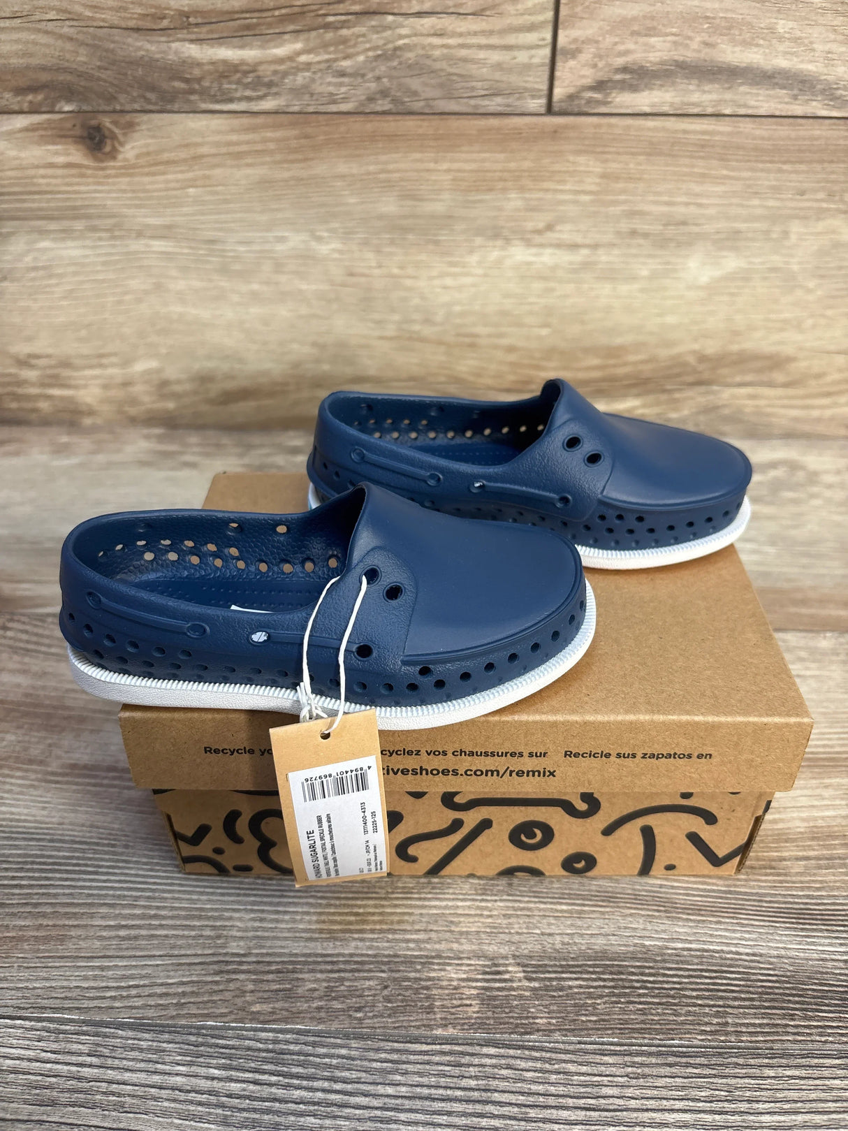 Blue kids slip-on clogs with ventilation holes on a shoe box, wooden background
