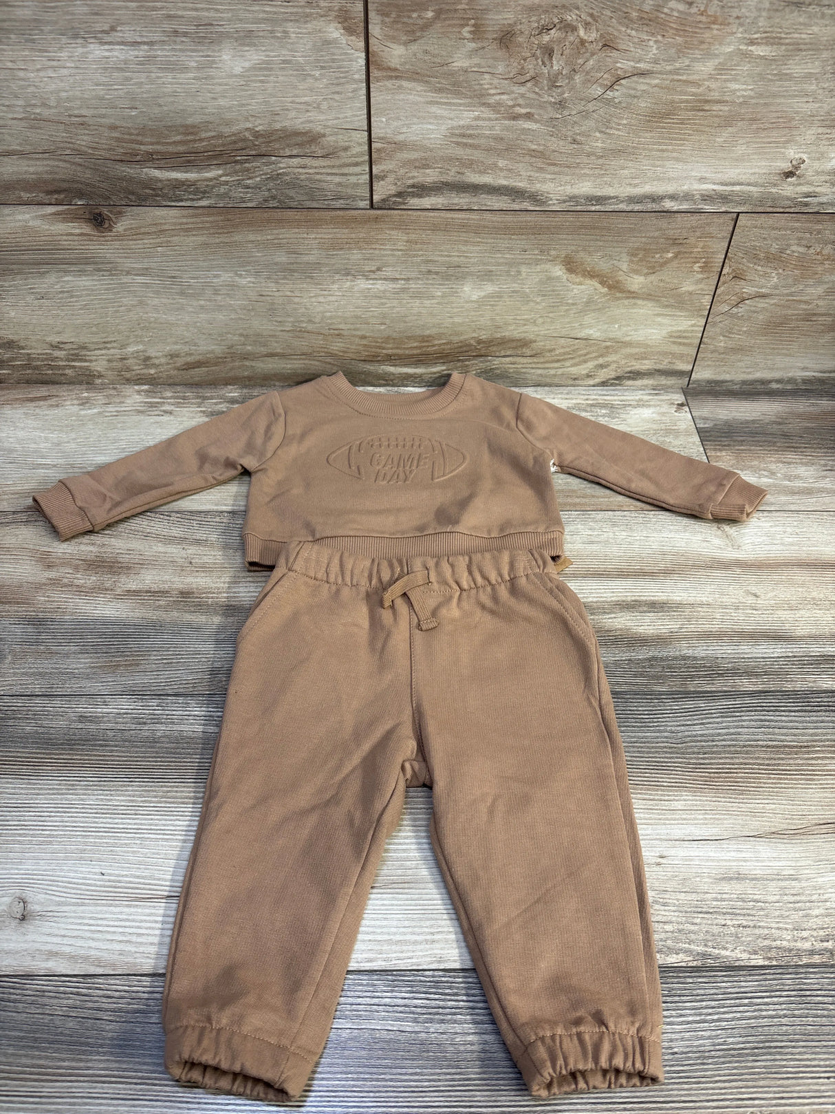 Flat lay of brown baby 2-piece sweatshirt and joggers with embossed GAME DAY motif, elastic waist and cuffs on wood background
