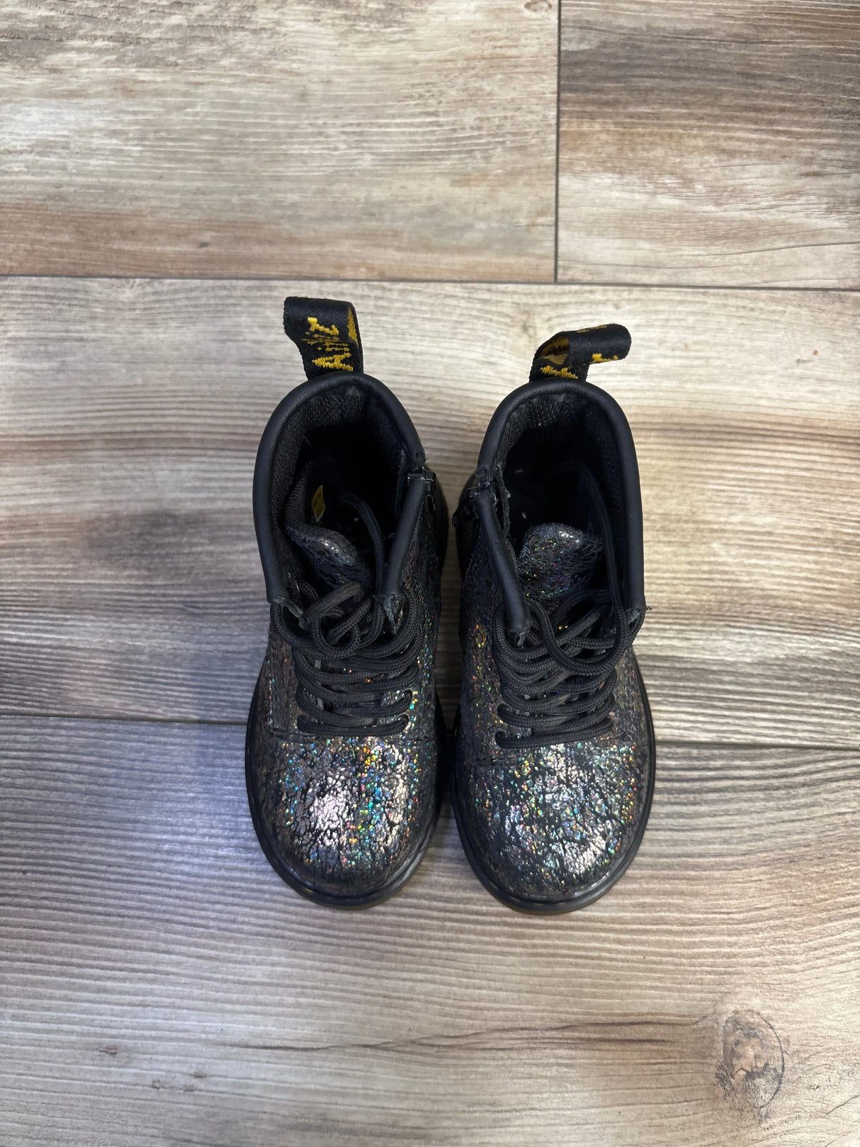 Top-down view of Dr. Martens 1460 boots size 7C showcasing black crinkle metallic finish, lace-up and pull tabs on wood floor