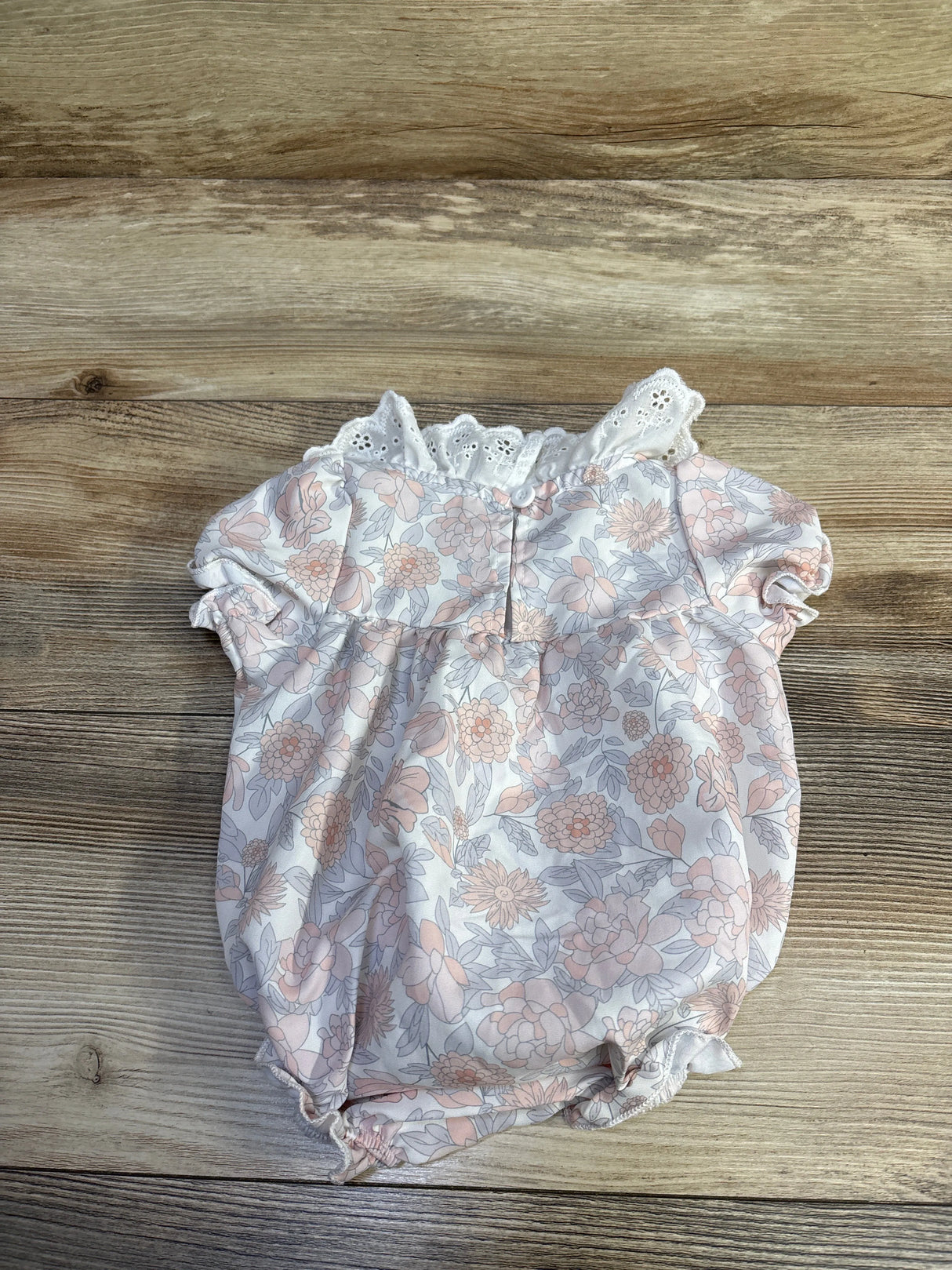 Flat-lay front view of baby bubble romper with eyelet collar and pink floral print on wood background