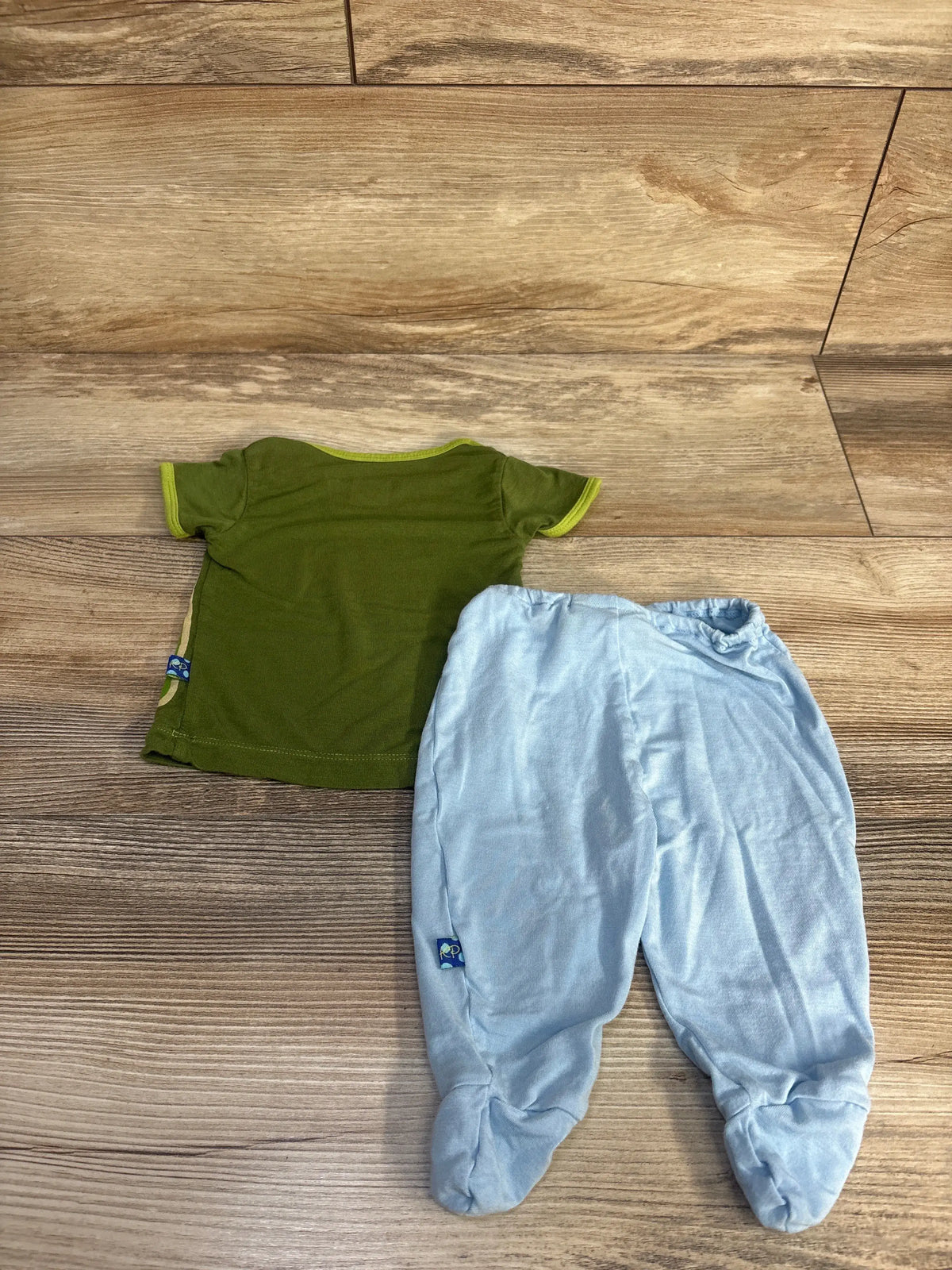 Top view of Kickee Pants two-piece bamboo shirt and footed pants set showcasing a green shirt and enclosed feet on wood flooring