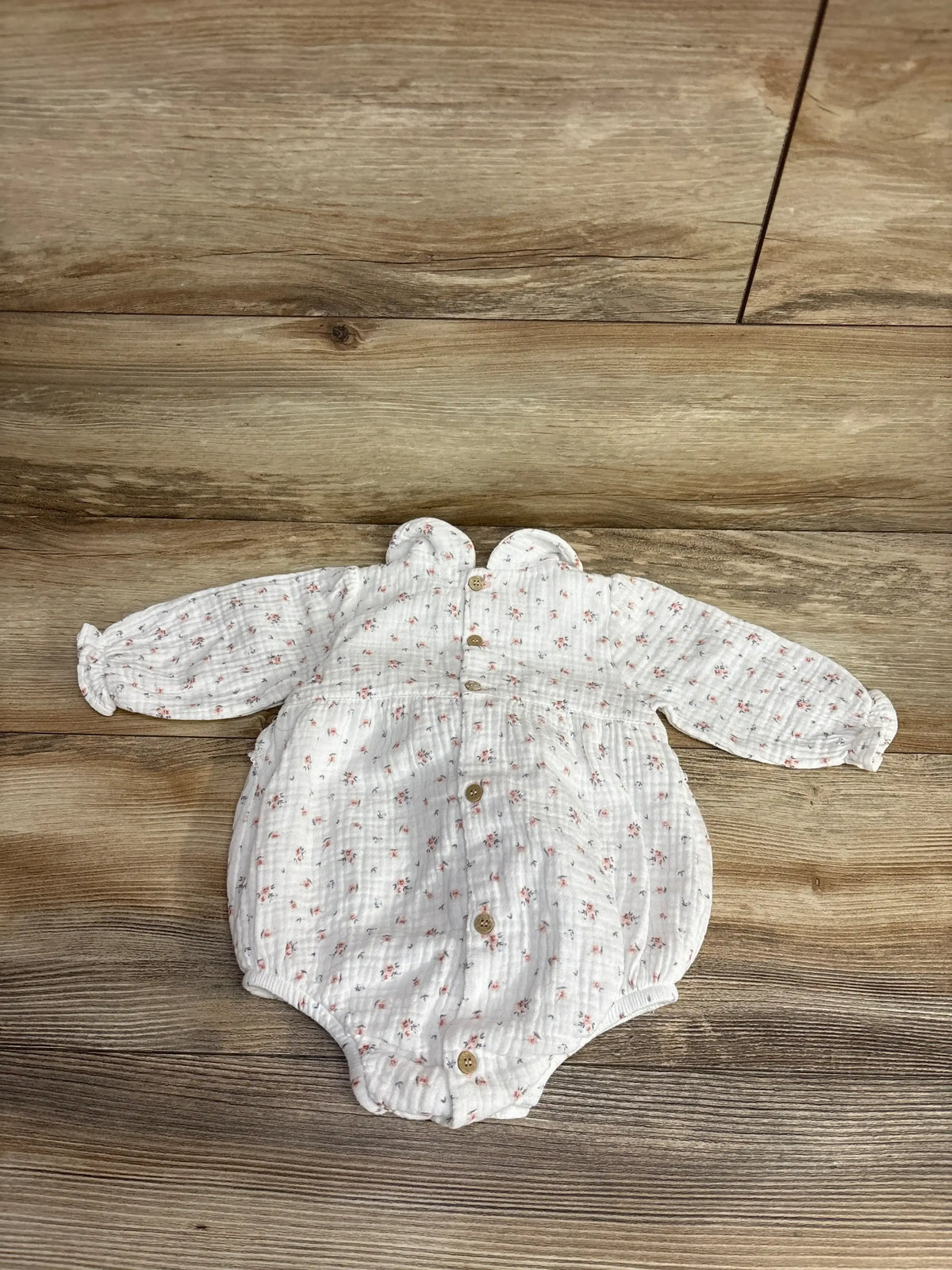White long-sleeve baby romper with small floral print and wooden buttons on wooden floor