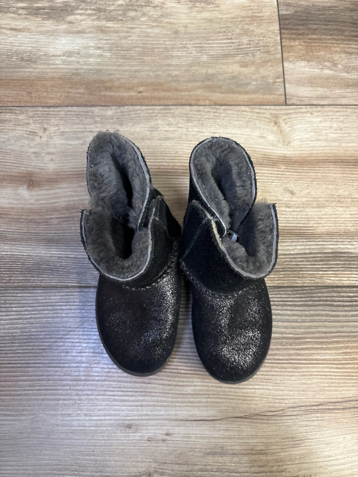 Top view of UGG Keelan metallic glitter boots showcasing black uppers and plush lining with a wood floor background