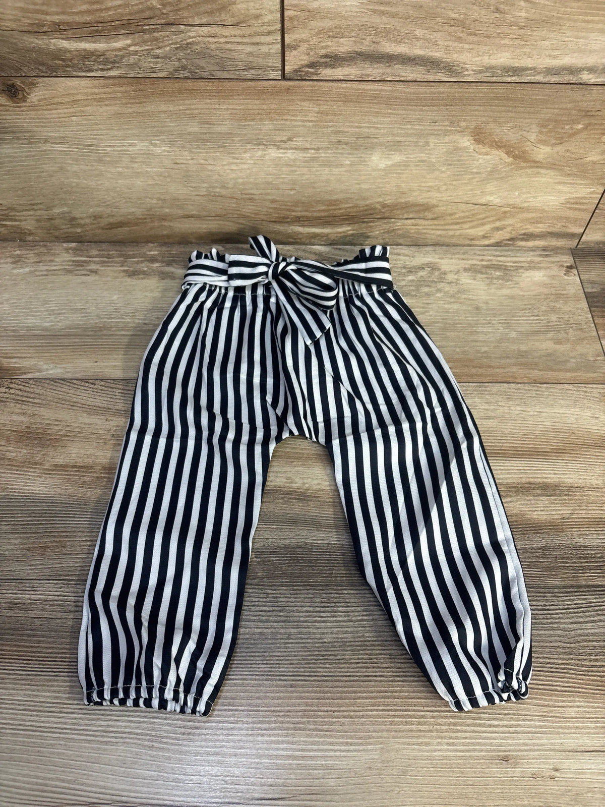 Front view of striped pull-on pants in white showcasing tie waist and elastic cuffs with a wood-look background