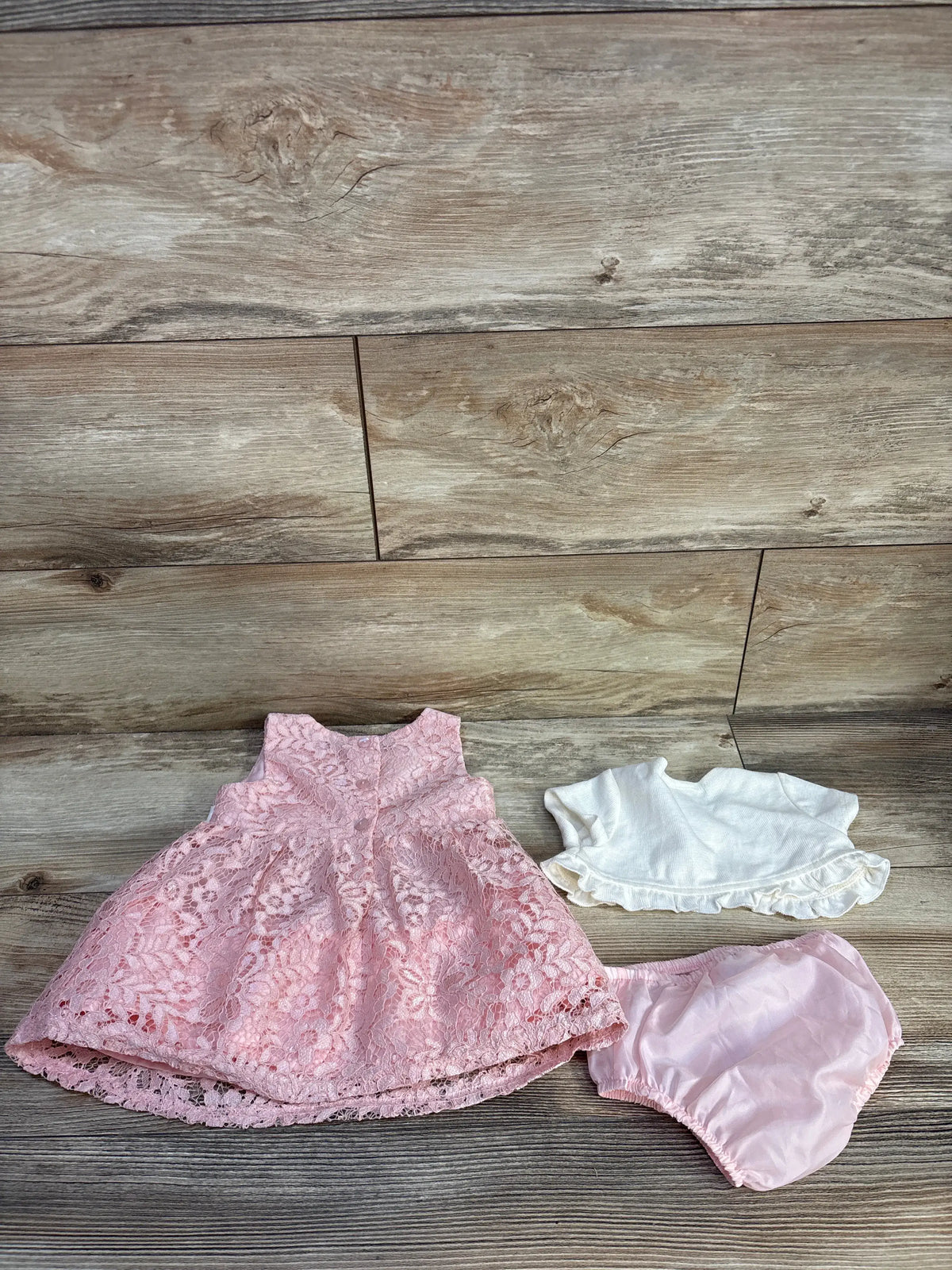 Top-down view of Bonnie Baby three-piece lace dress set with pink lace dress, bloomers, and white cardigan