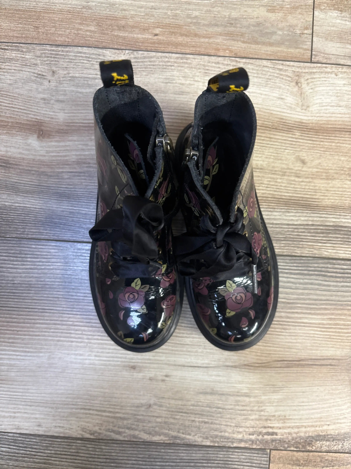 Top view of Dr. Marten 1460 Decayed Rose boots with black floral rose print, ribbon laces, and pull tabs on a wood floor
