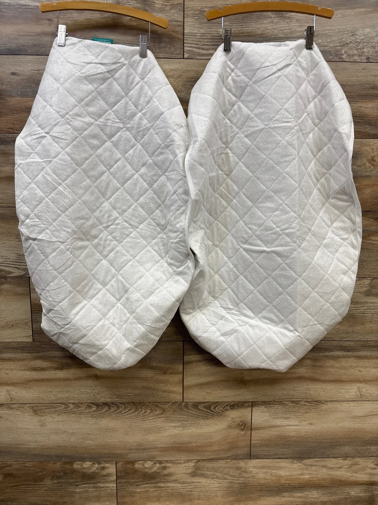 Pair of white quilted baby bassinet mattress pads on wooden floor