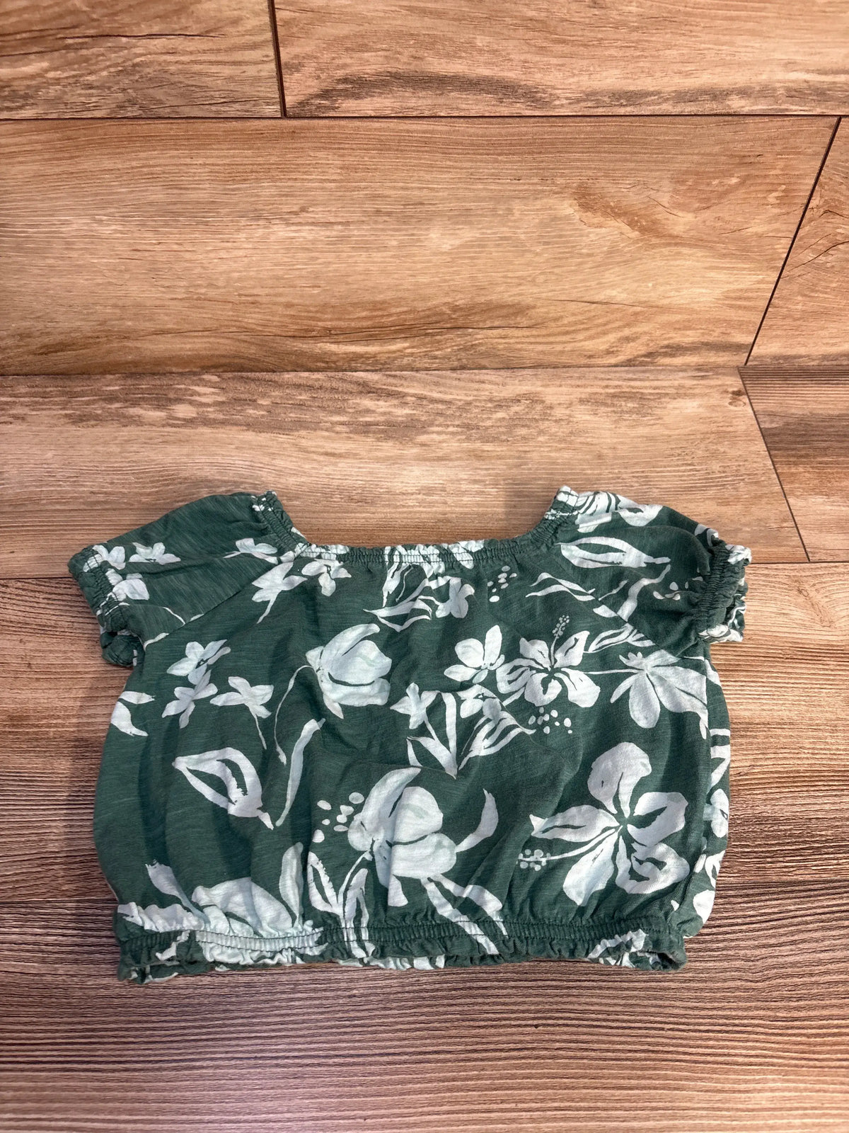 Green floral cropped top for kids with white flower print on a wood background