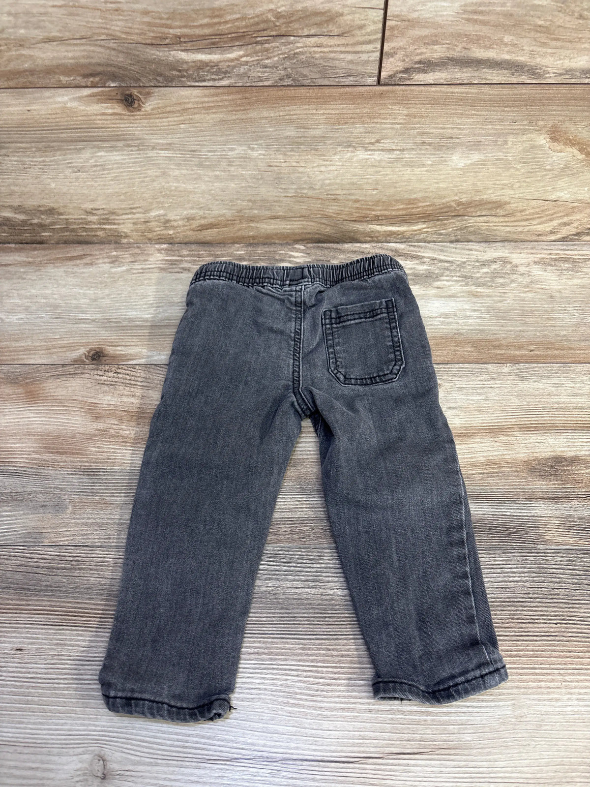 Back view of Oshkosh grey drawstring jeans in size 18 months showcasing a drawstring waist and back pocket on wood flooring
