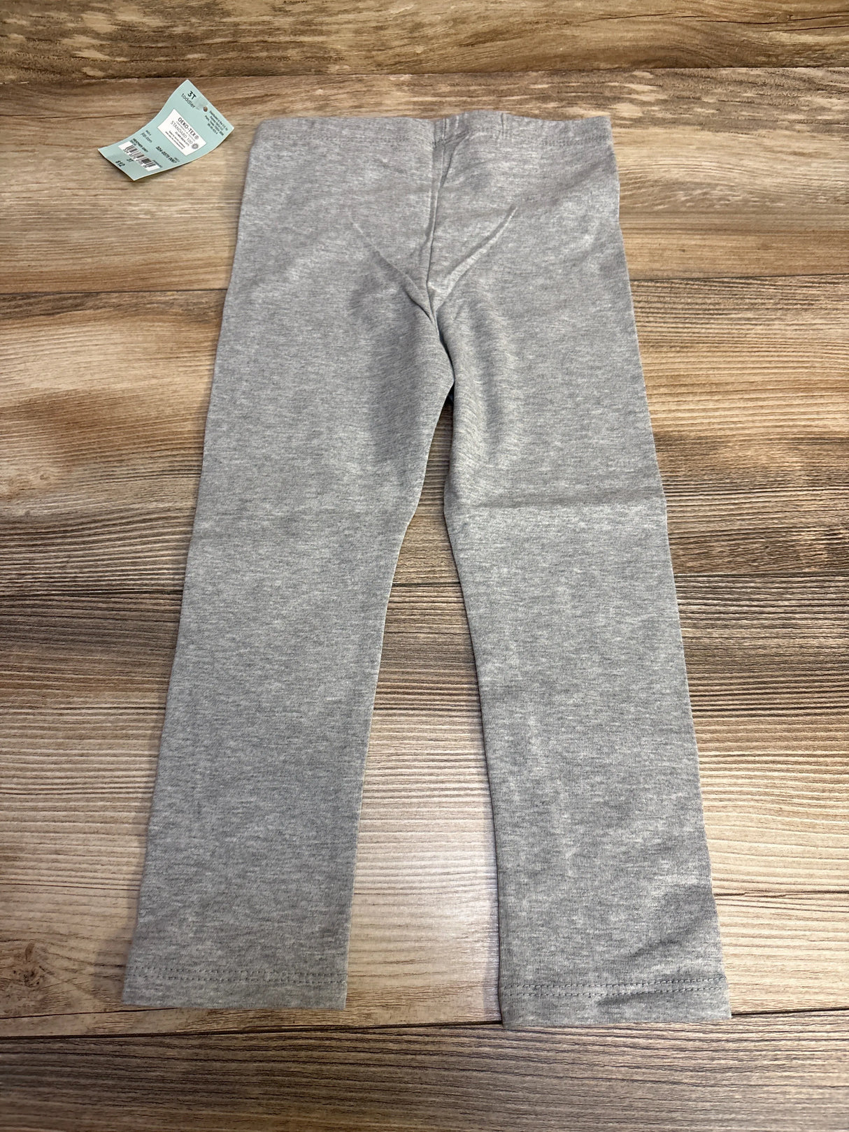 Gray toddler leggings on wooden floor with clothing tag nearby