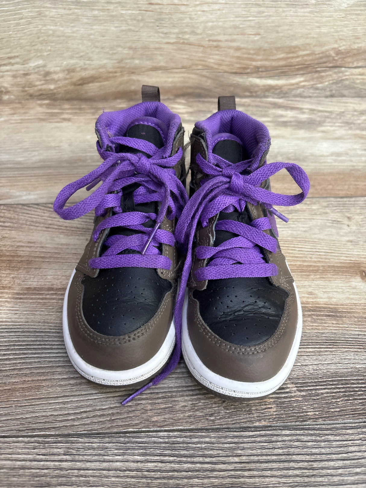 Pair of children's brown and black sneakers with purple laces on wooden floor