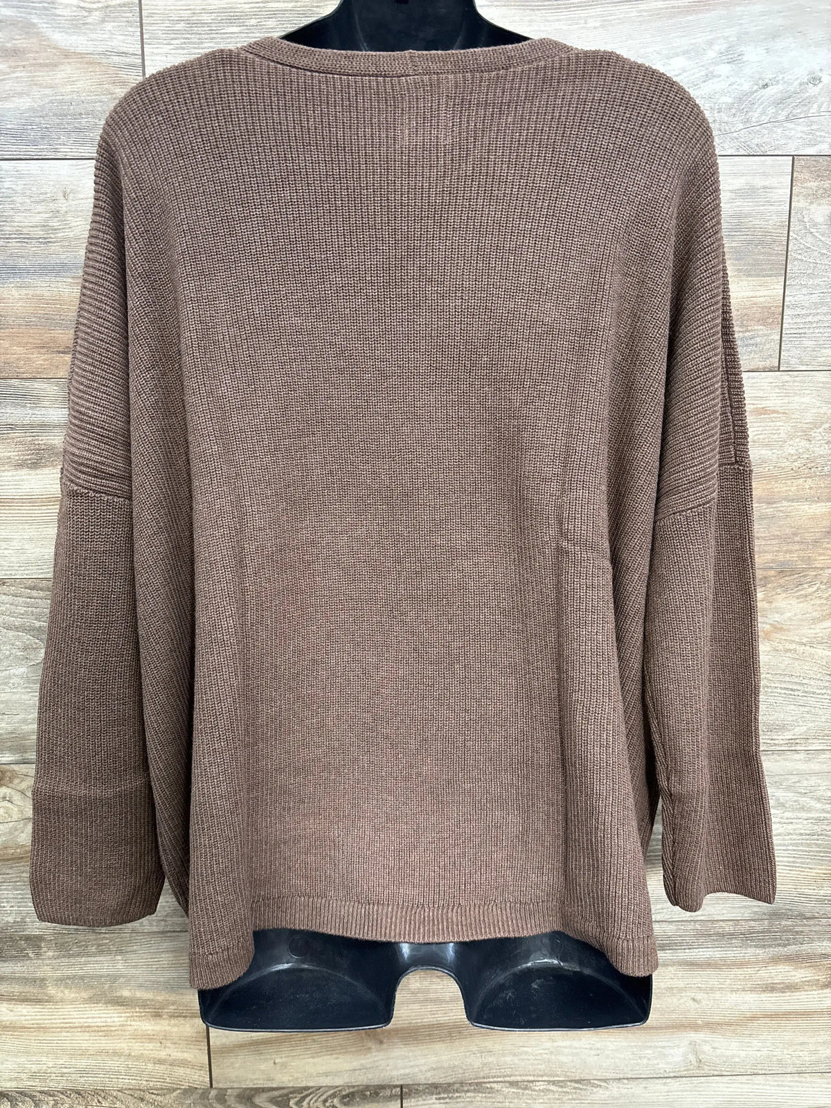 Brown knit sweater with long sleeves displayed on a black mannequin against a wood plank background