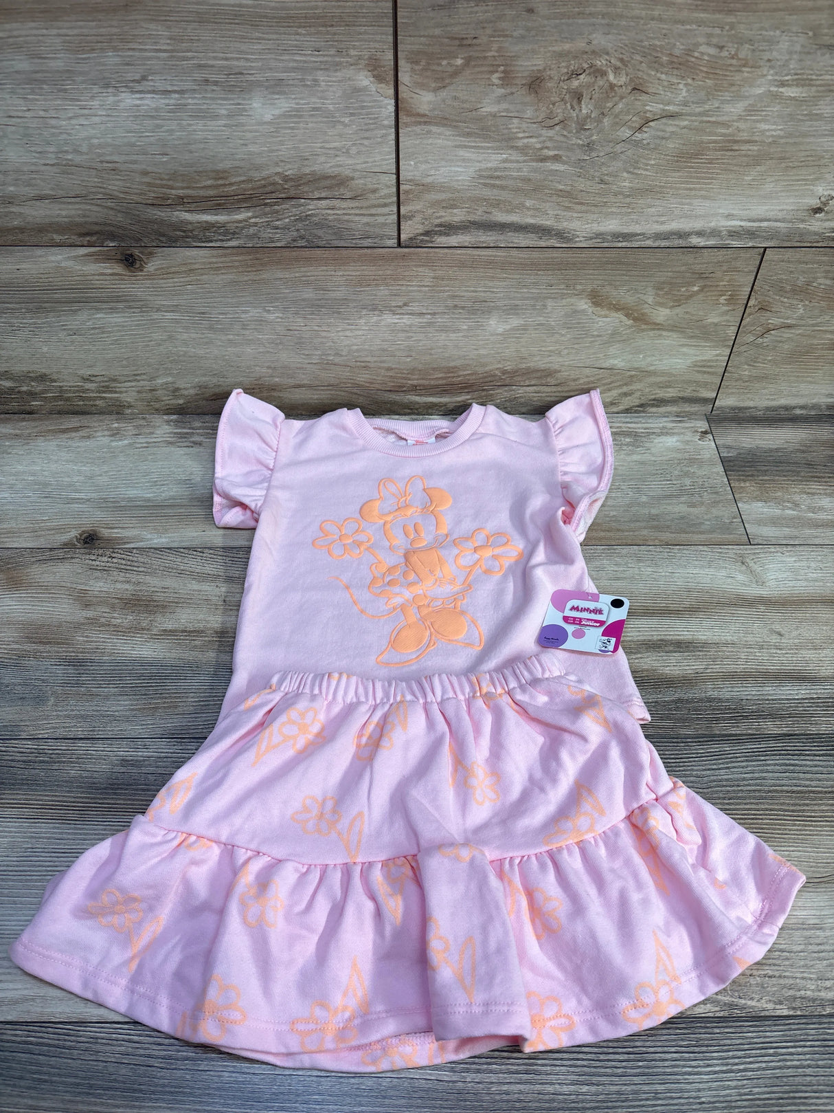 Top-down of pink Disney Minnie Mouse 2-piece shirt and tiered skort with Minnie graphic and elastic waist on wood background