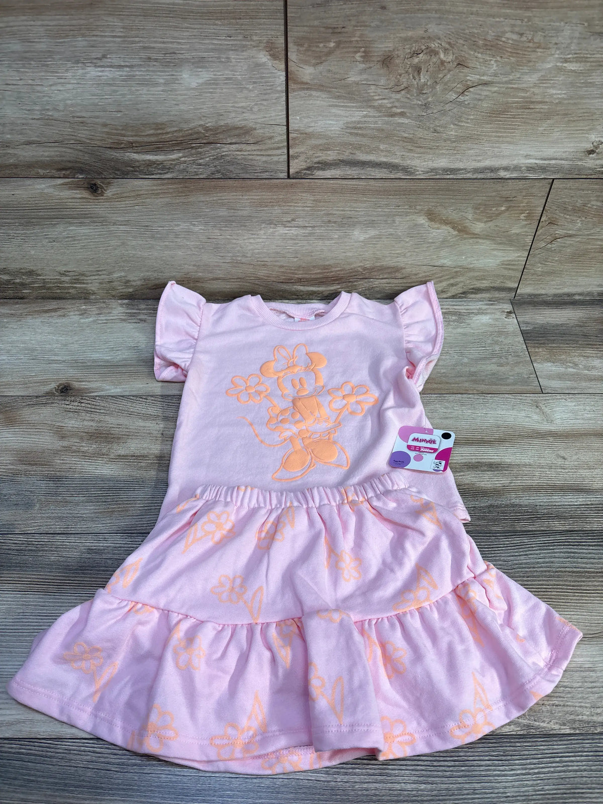 Top-down of pink Disney Minnie Mouse 2-piece shirt and tiered skort with Minnie graphic and elastic waist on wood background