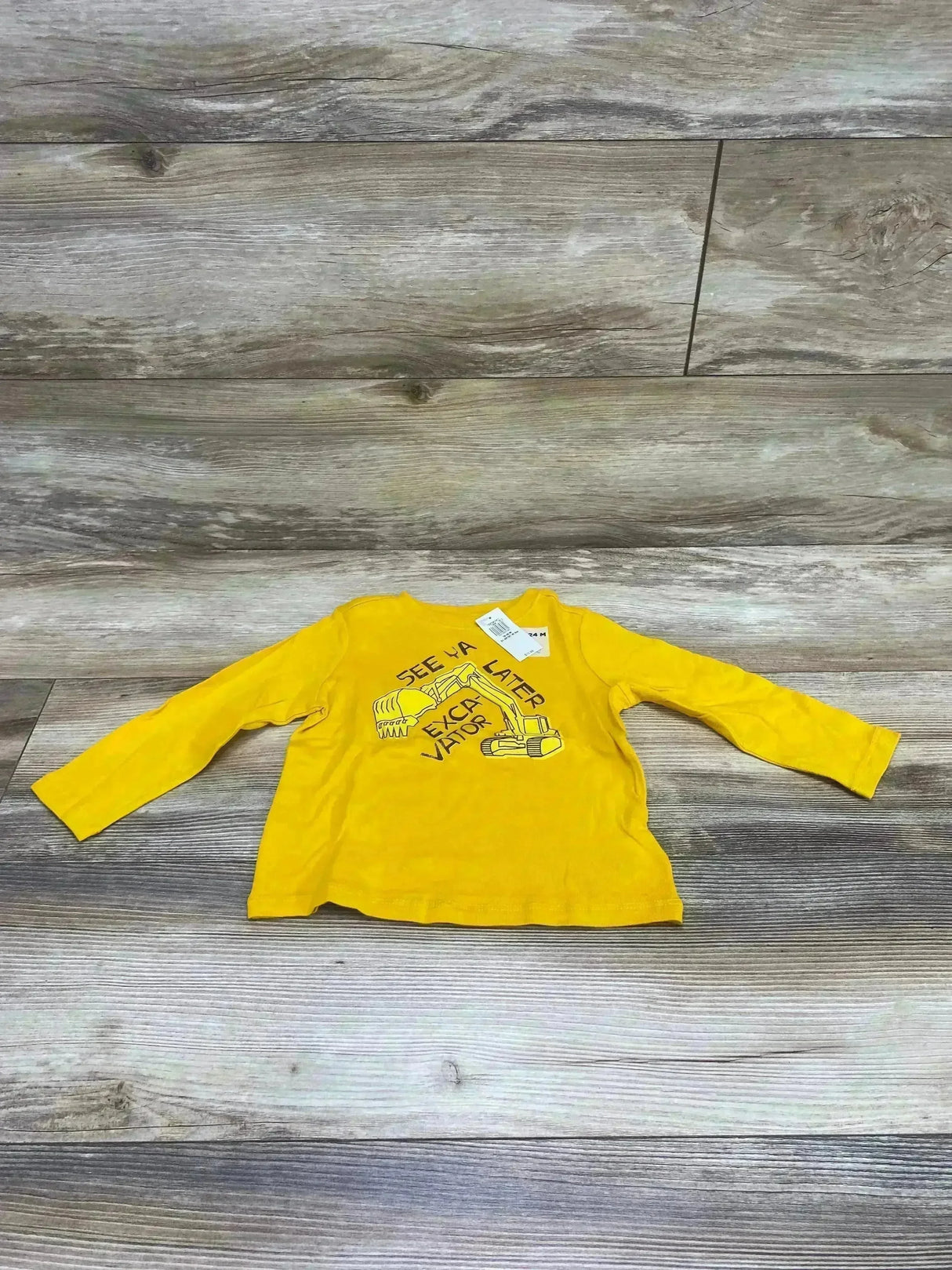 Front view of Old Navy yellow toddler long-sleeve shirt 18-24 months with excavator print and SEE YA LATER text on wood floor