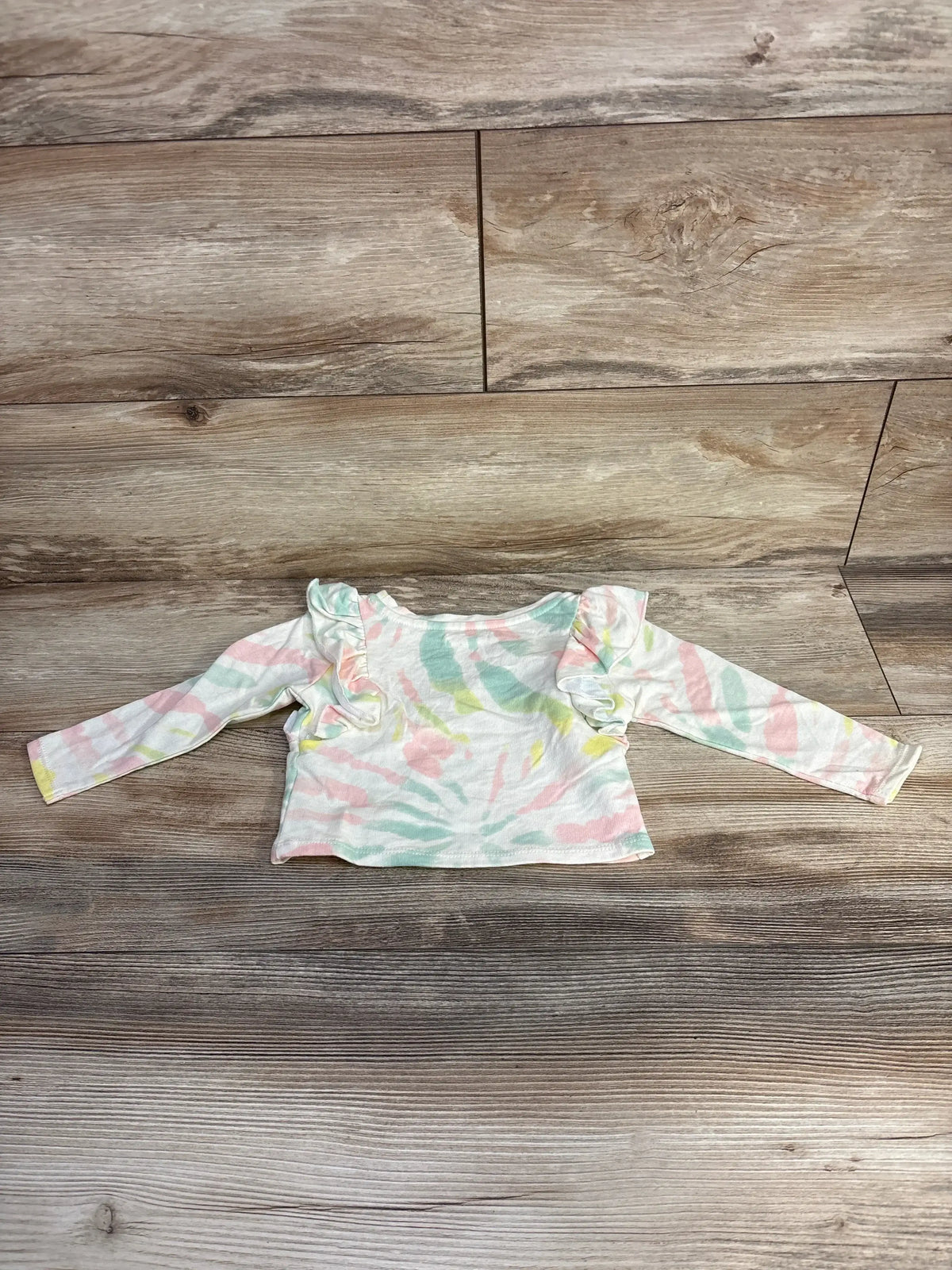 Pastel tie-dye long sleeve baby shirt with ruffle details on shoulders laid on wooden floor