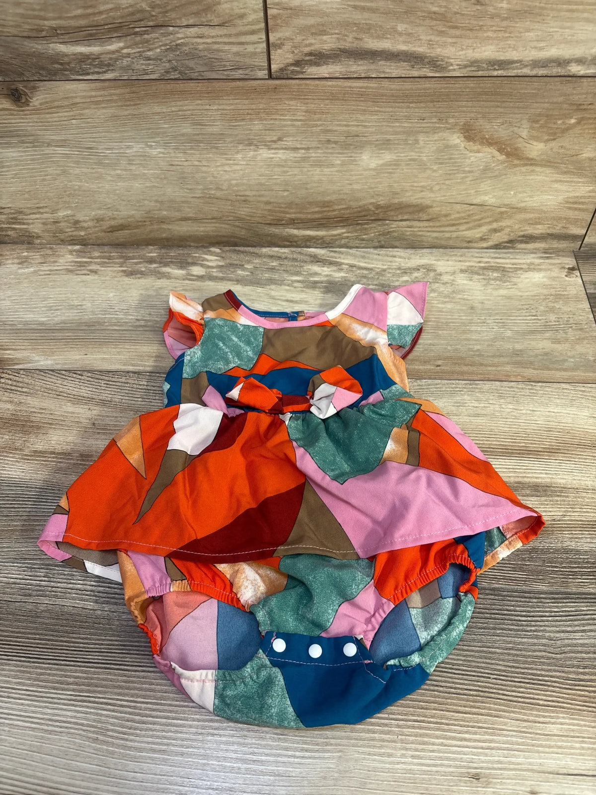Top view of PatPat bodysuit dress, size 6-9m, showcasing multicolor panels and bottom snaps on a wood-look floor