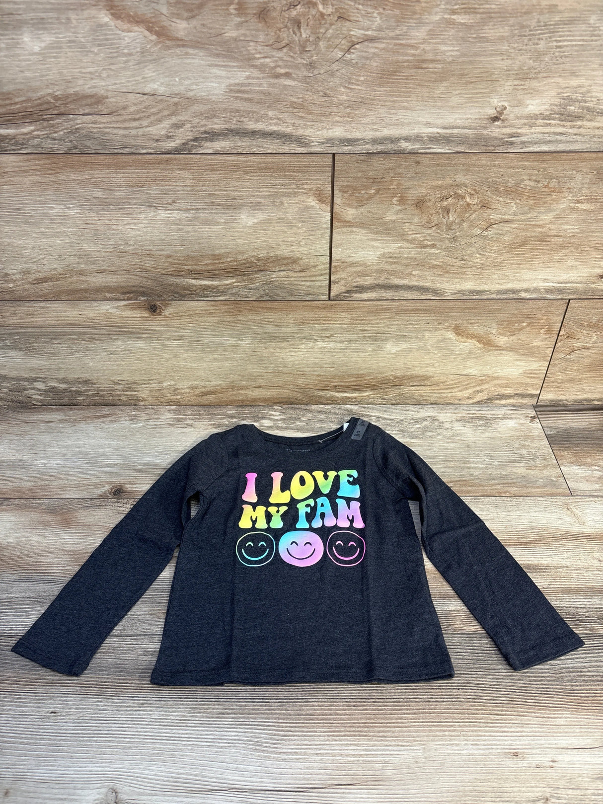 Kids' black long sleeve shirt with 'I Love My Fam' and colorful smiley faces on wood floor