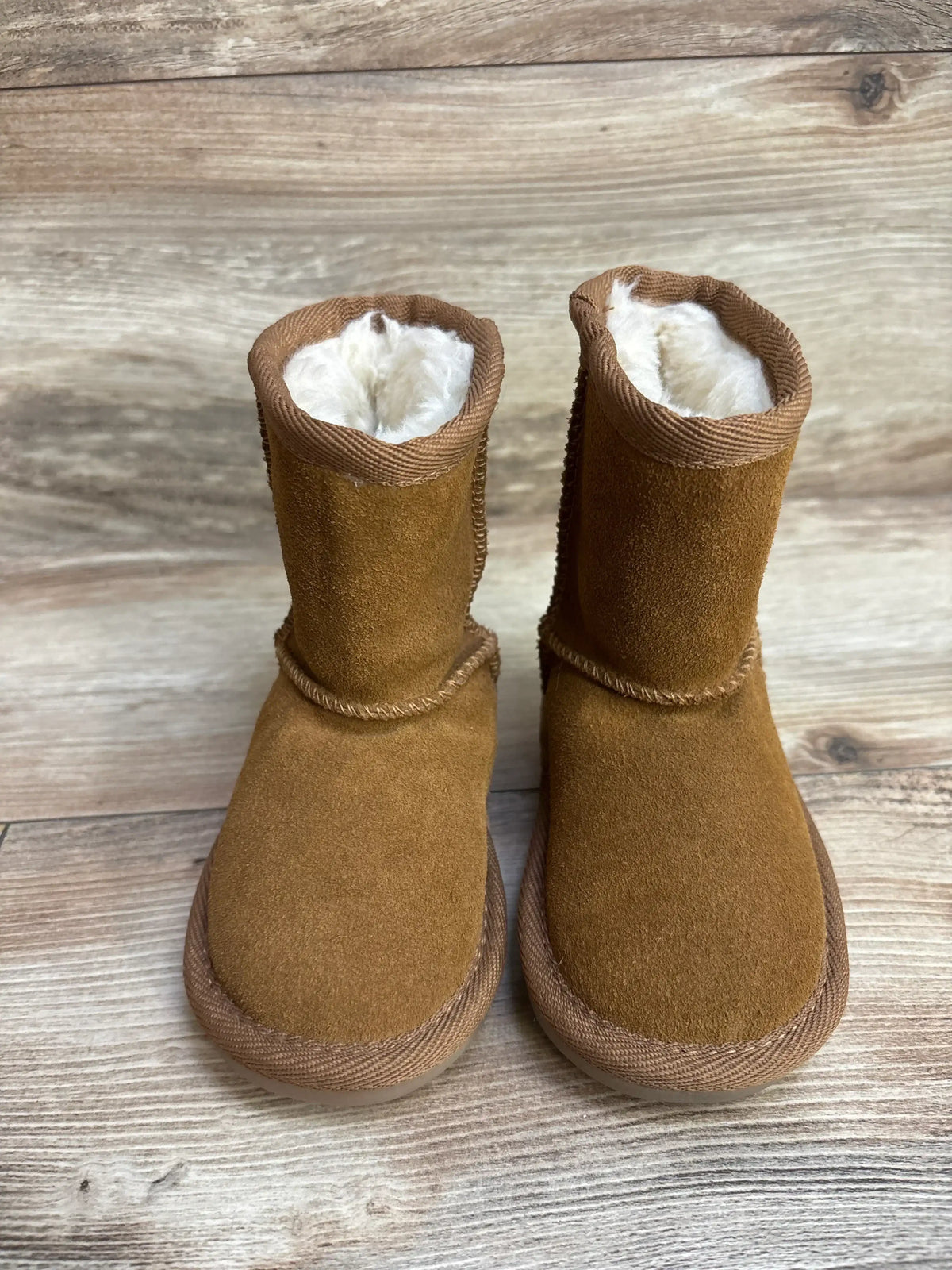 Pair of brown suede winter boots with white fur lining on wooden floor
