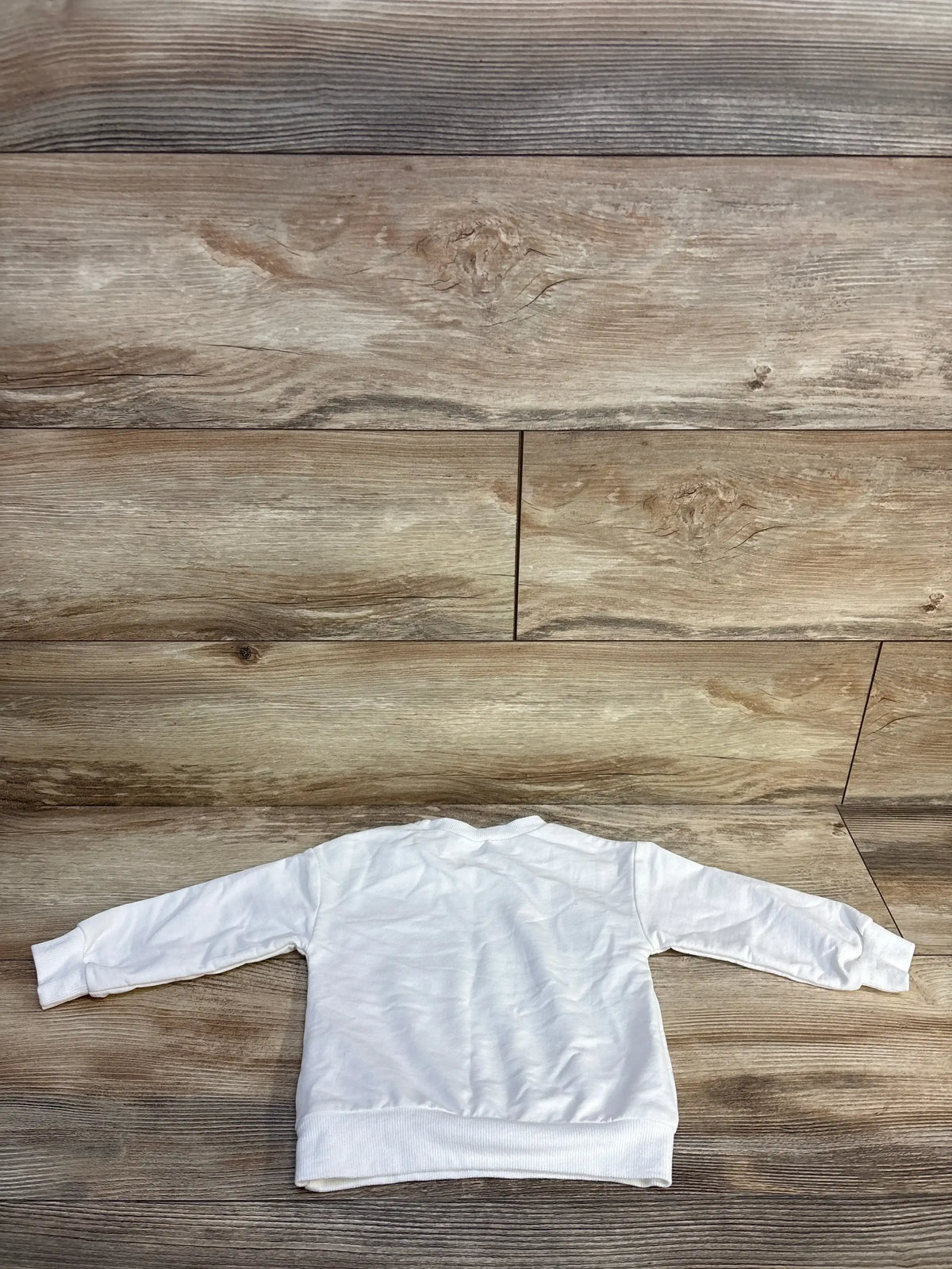 White long sleeve toddler sweatshirt displayed flat on wood background