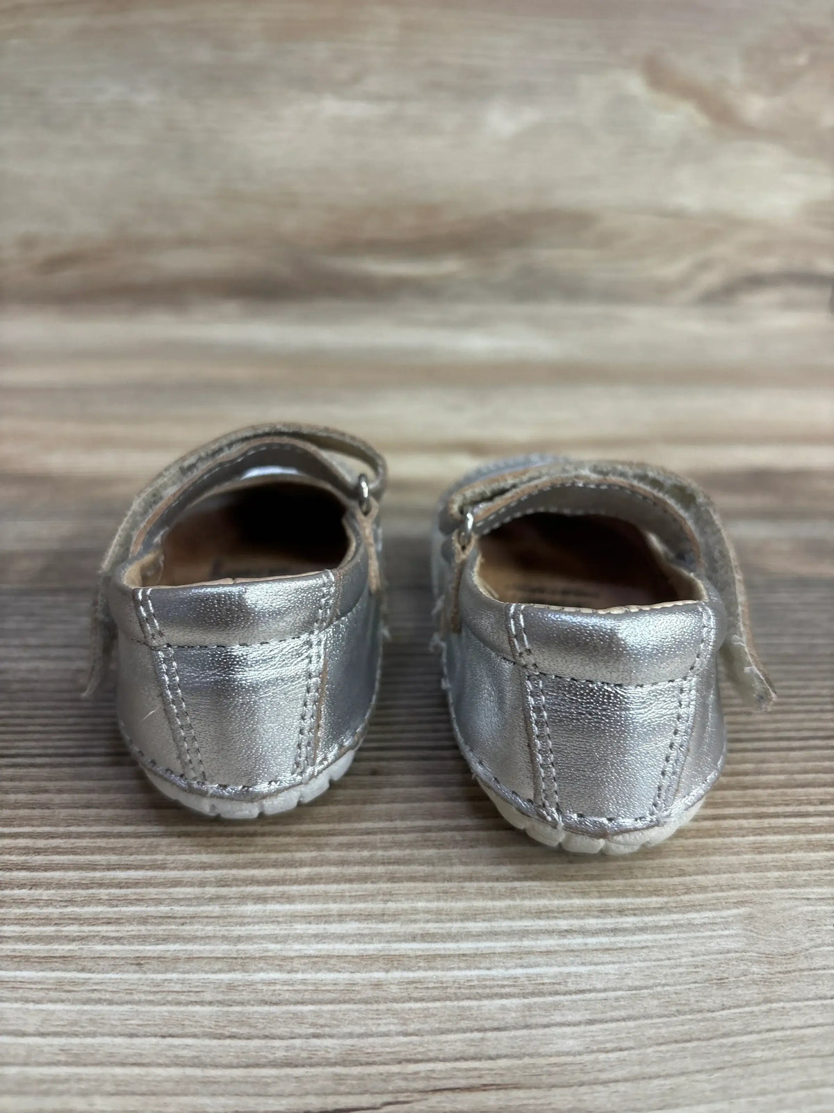Pair of silver metallic toddler shoes with velcro straps on wood surface