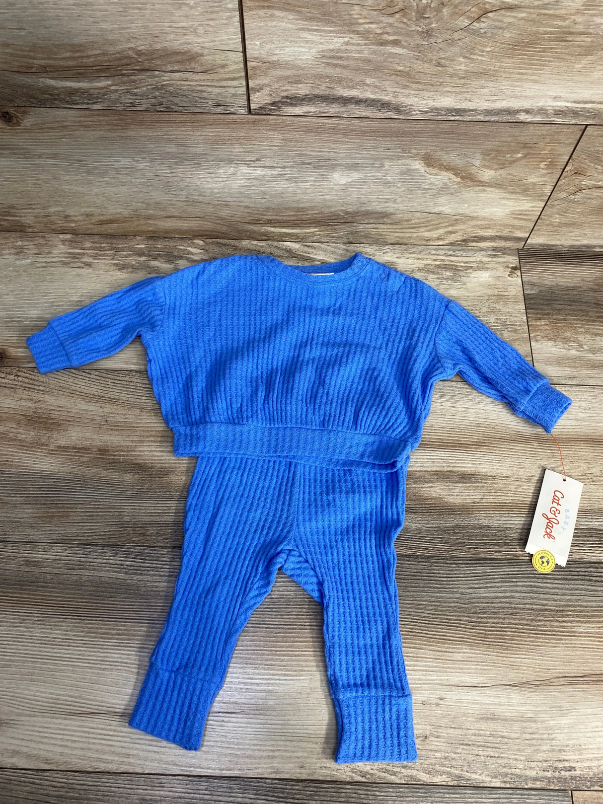 Blue textured baby outfit with long sleeves and pants laid on wooden floor, Cat & Jack brand tag