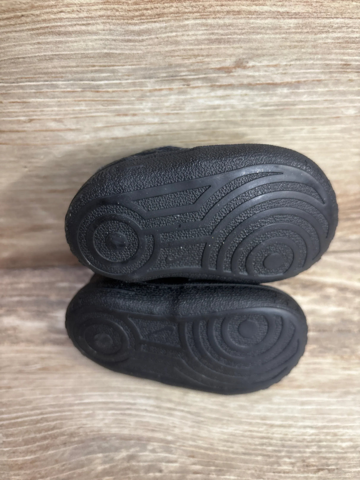Pair of black toddler shoes with textured soles on wooden surface
