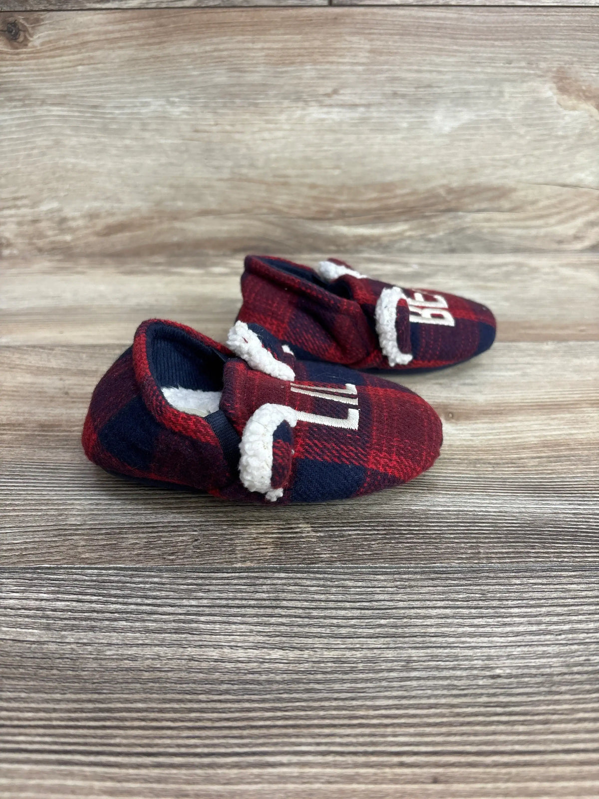 Red and navy plaid baby booties with white fleece lining on wooden background