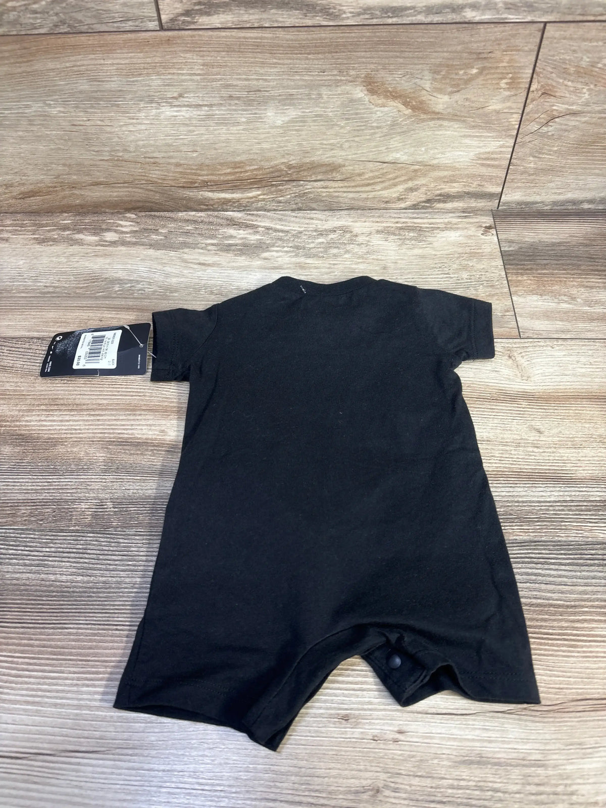 Flat lay back view of black Nike shortie romper size 3M showcasing snap crotch and short sleeves on wood floor background