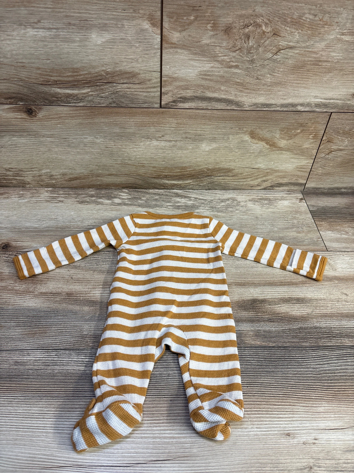 Flat lay of Just One You waffle knit newborn sleeper with mustard and white stripes and built-in footies on wood