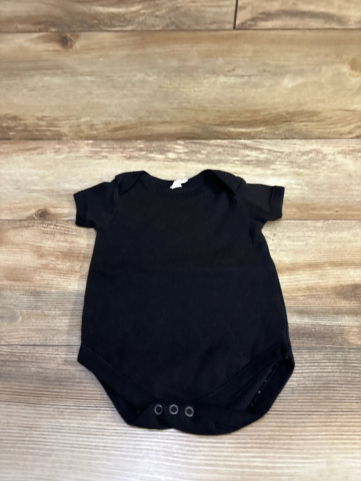 Flat lay of black Baby Jay bodysuit size 6-12 months showing three snap closures and envelope shoulders on wood background