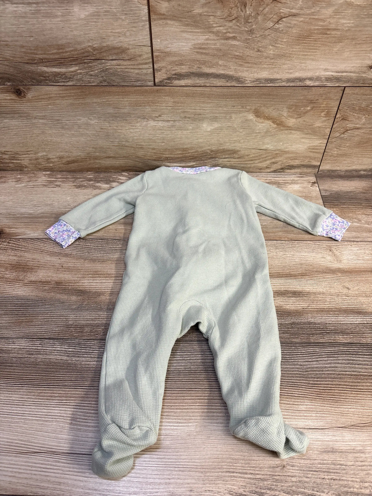 Front view of Just One You green waffle knit sleeper with floral trim and covered feet on a wood background