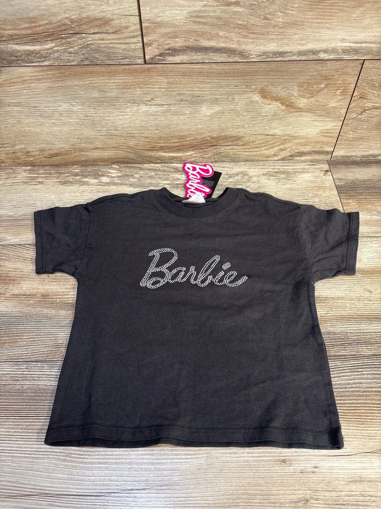 Black kids Barbie t-shirt with rhinestone logo, laid flat on wooden surface