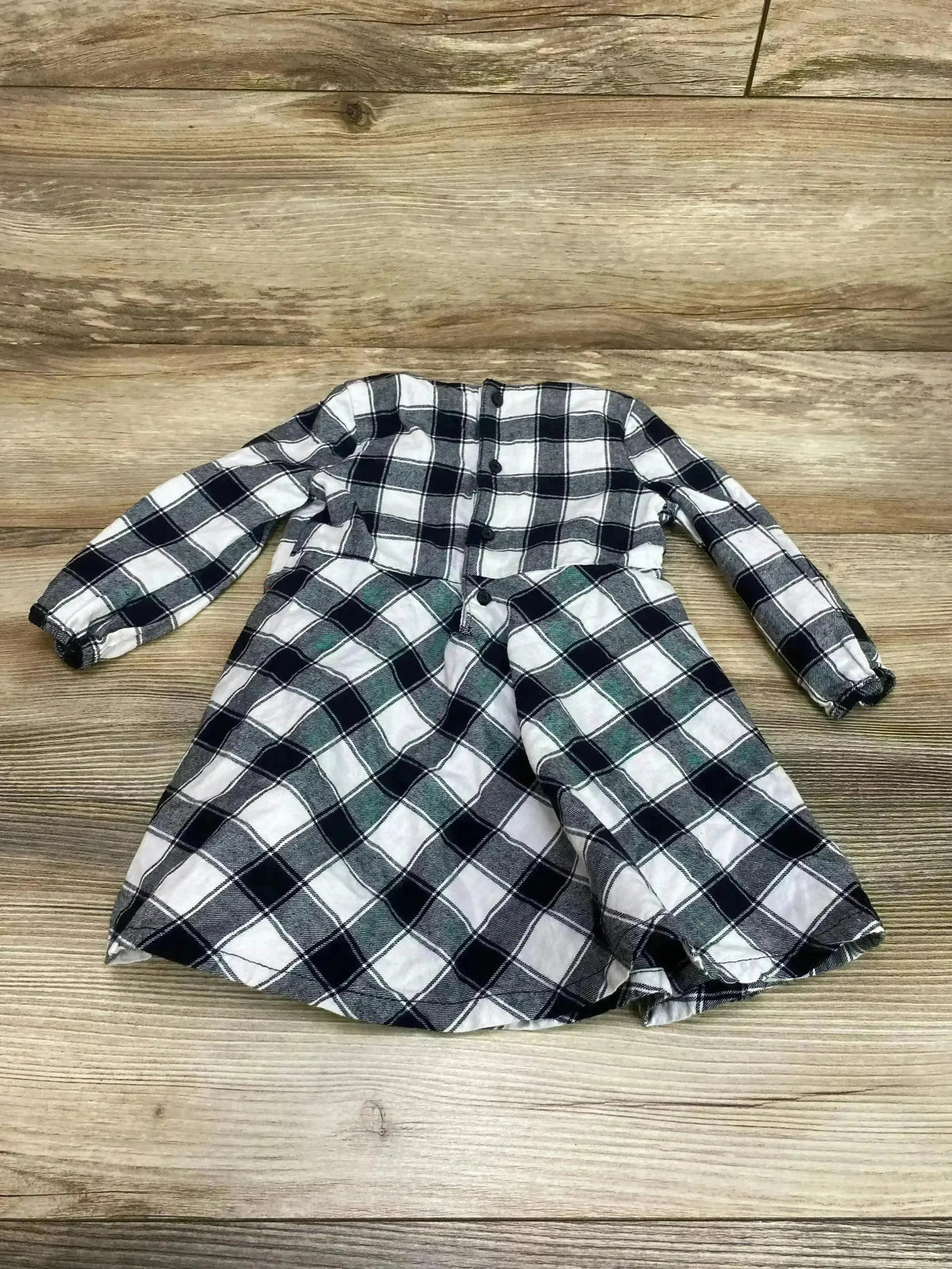 Flat-lay of Just One You Buffalo Check dress in white and black with button-front bodice and gathered skirt on wood floor