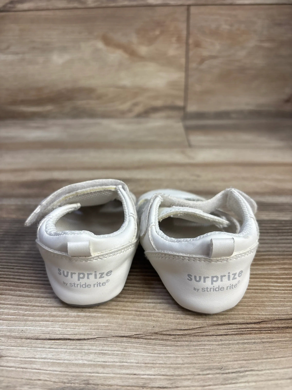 Rear view of white Surprize by Stride Rite fisherman sandals, size 3C, showing adjustable ankle straps on a wood surface