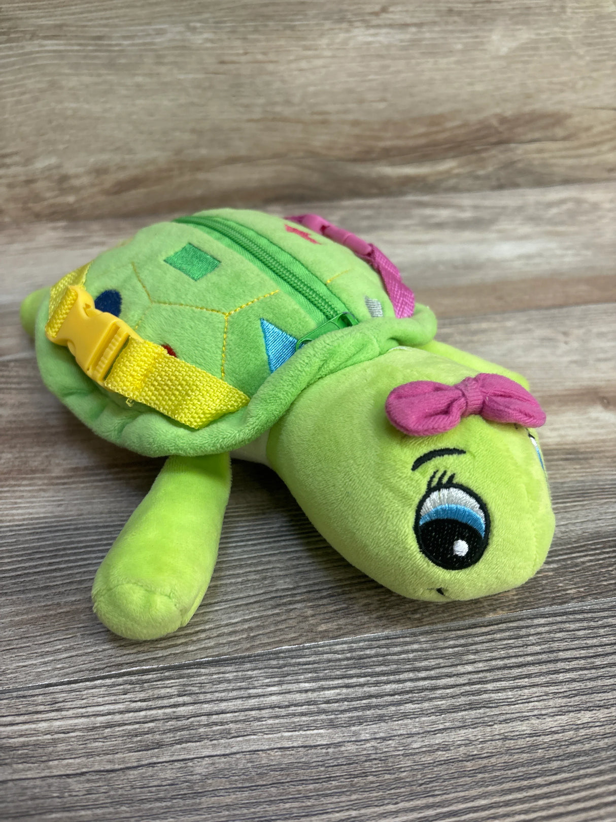 Plush green turtle backpack with zipper and yellow buckle on wooden surface