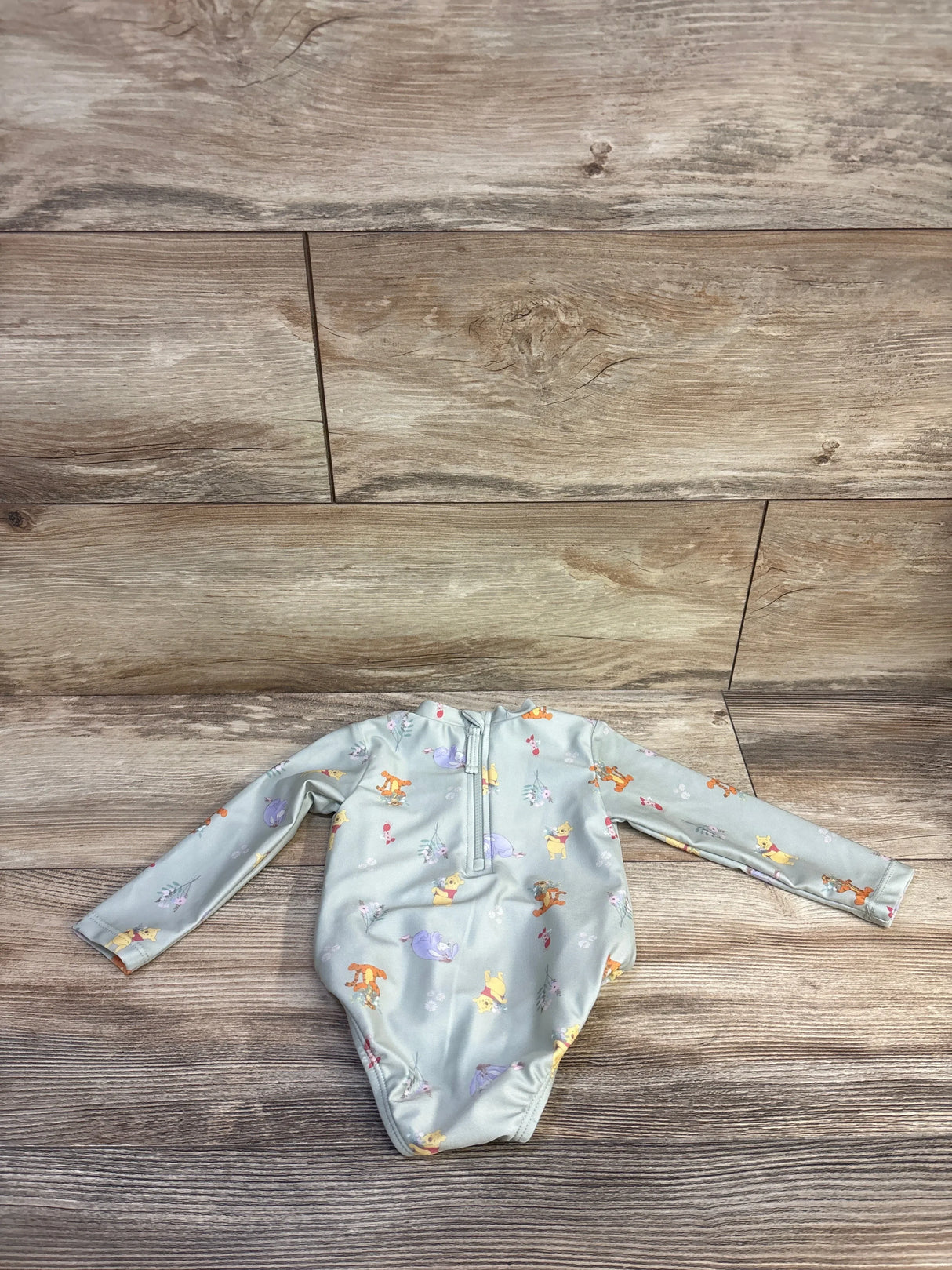 Top down of green Winnie the Pooh baby rashguard size 9M showing back zipper and all over print on wood background