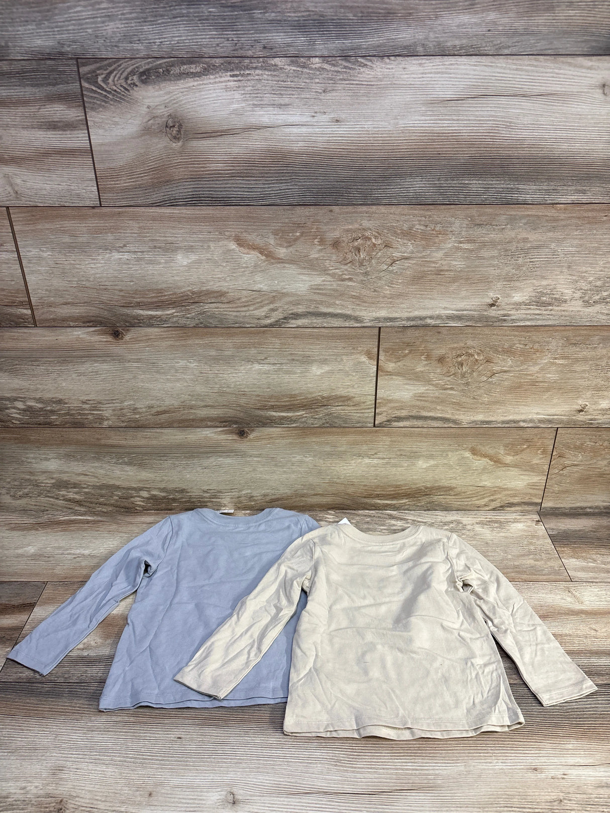 Flat lay of two Cat & Jack long-sleeve toddler shirts (beige and light blue), size 3T, showing fronts on wood floor